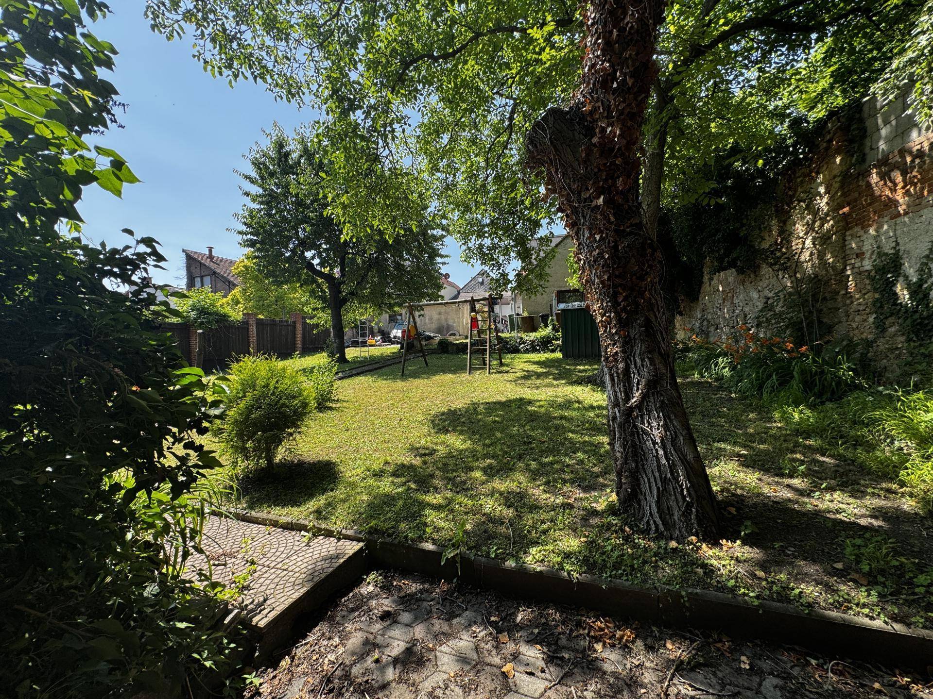 Grüner Gartenbereich mit Rasenfläche, Bäumen und einem kleinen Spielplatz im Hintergrund.