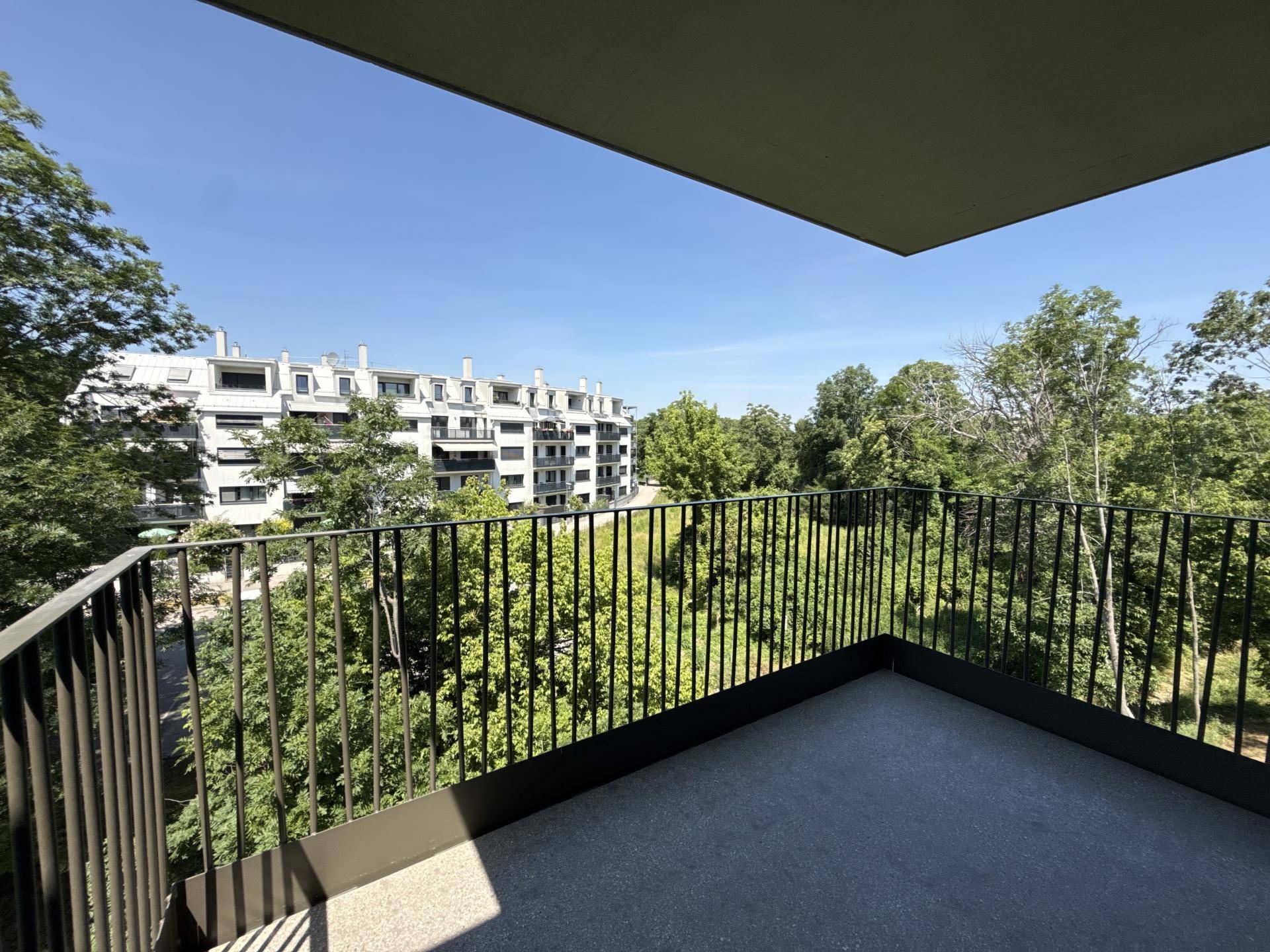 Geräumiger Balkon mit Metallgeländer und weitem Blick ins Grüne sowie auf ein Wohngebäude.
