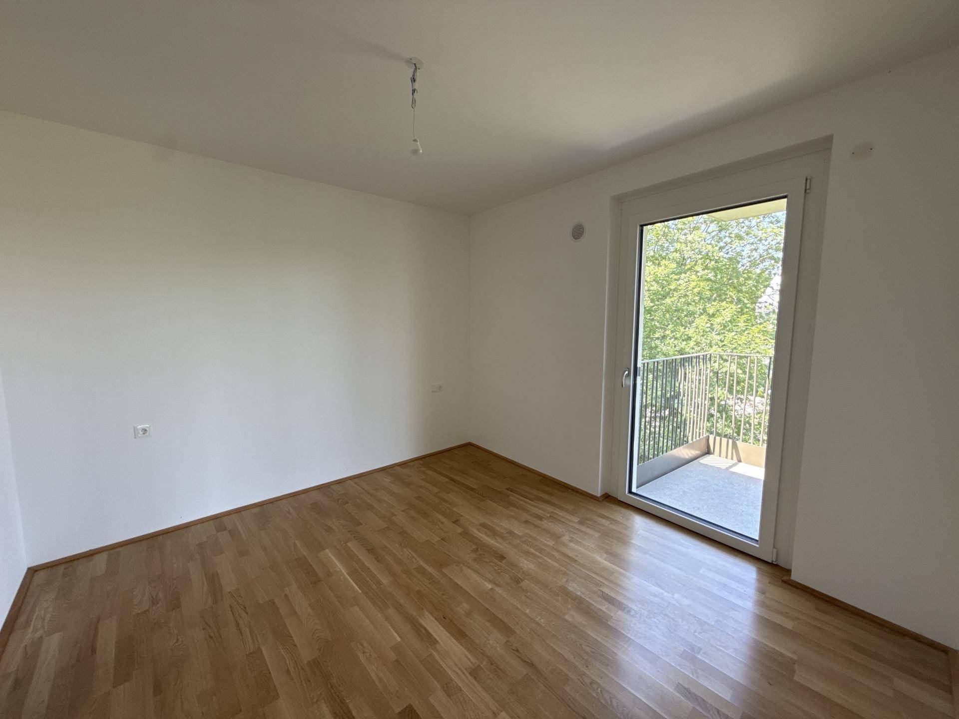 Helles Schlafzimmer mit Holzboden und Zugang zu einem privaten Balkon mit Grünblick.