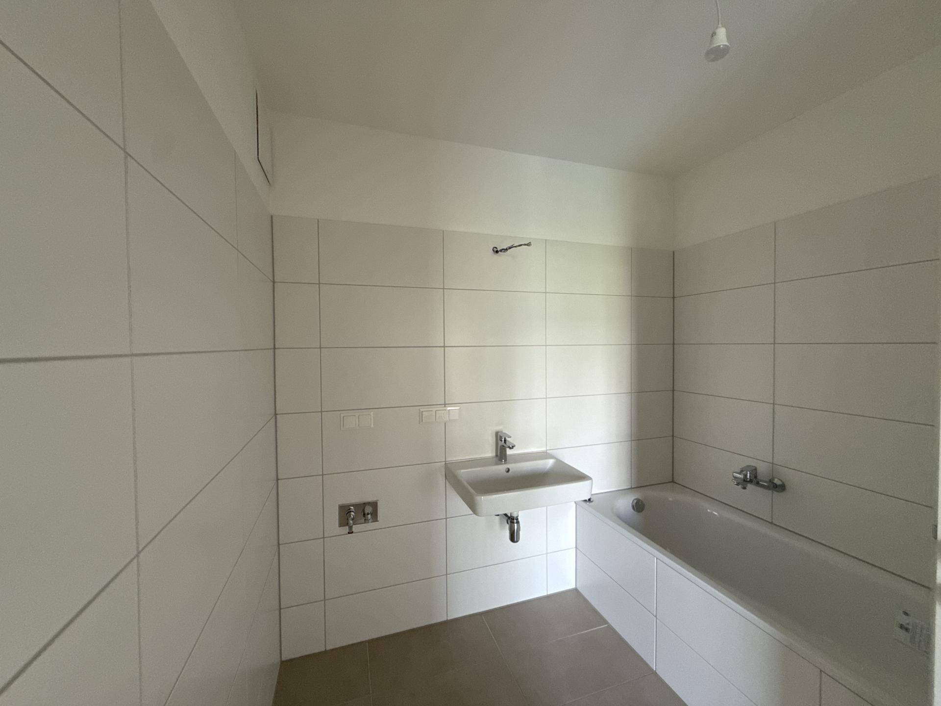 Modernes Badezimmer mit weißen Fliesen, Waschbecken und Badewanne, bereit zur Fertigstellung.