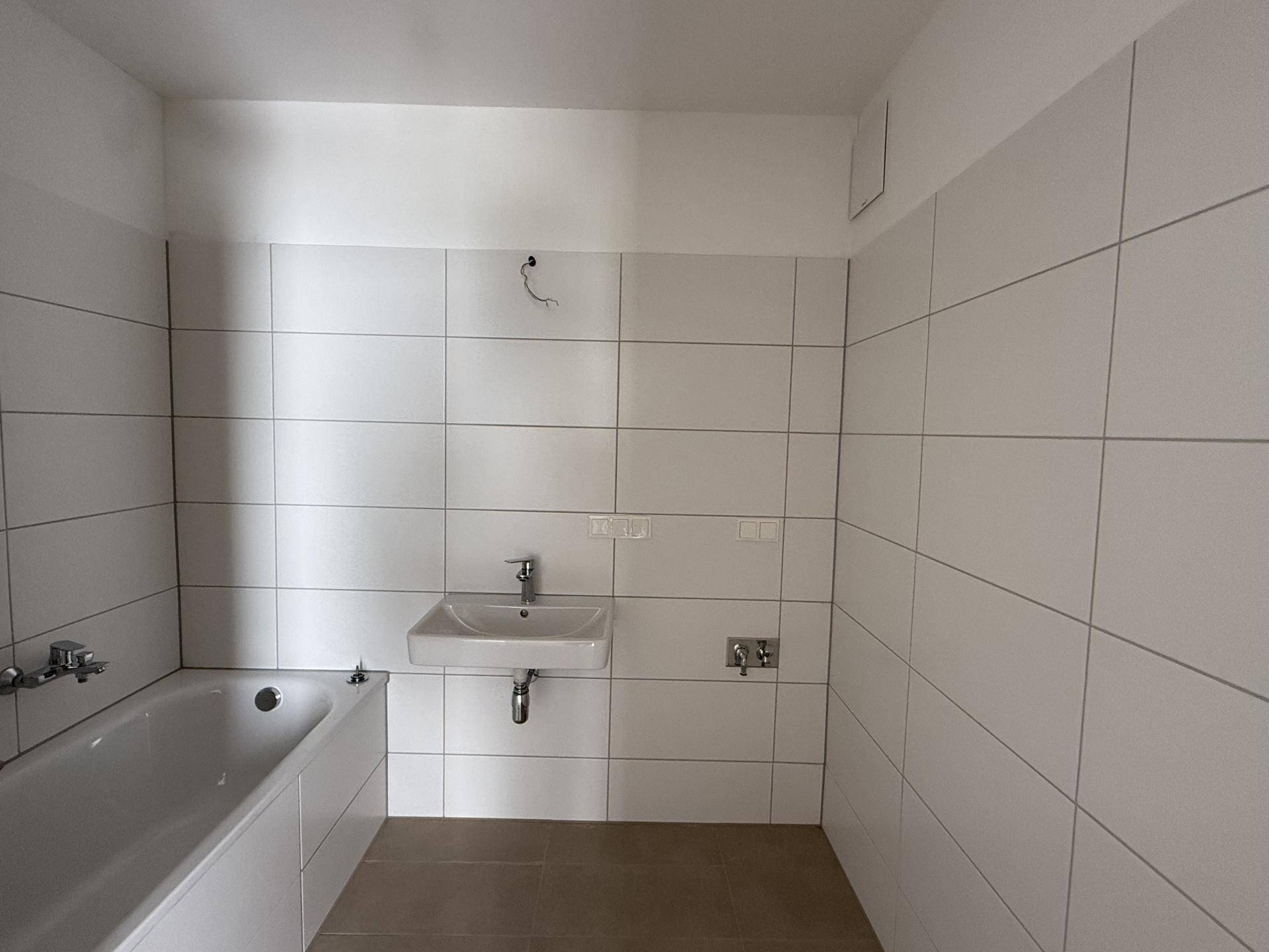 Modernes Badezimmer mit weißen Fliesen, Badewanne und Waschbecken, bereit für die Endmontage.