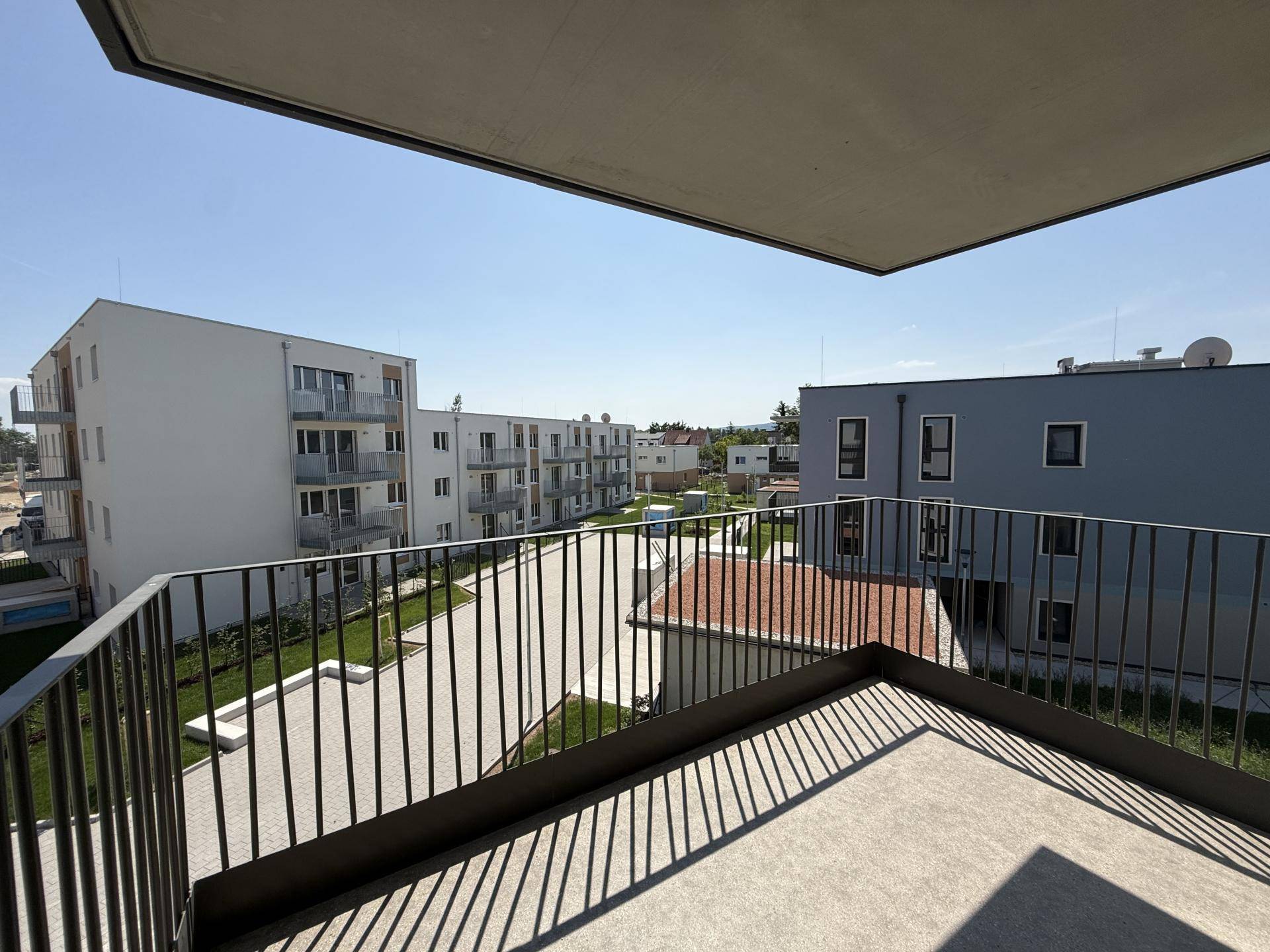 Balkon mit Metallgeländer und Blick auf die modernen Wohngebäude und die grüne Umgebung.