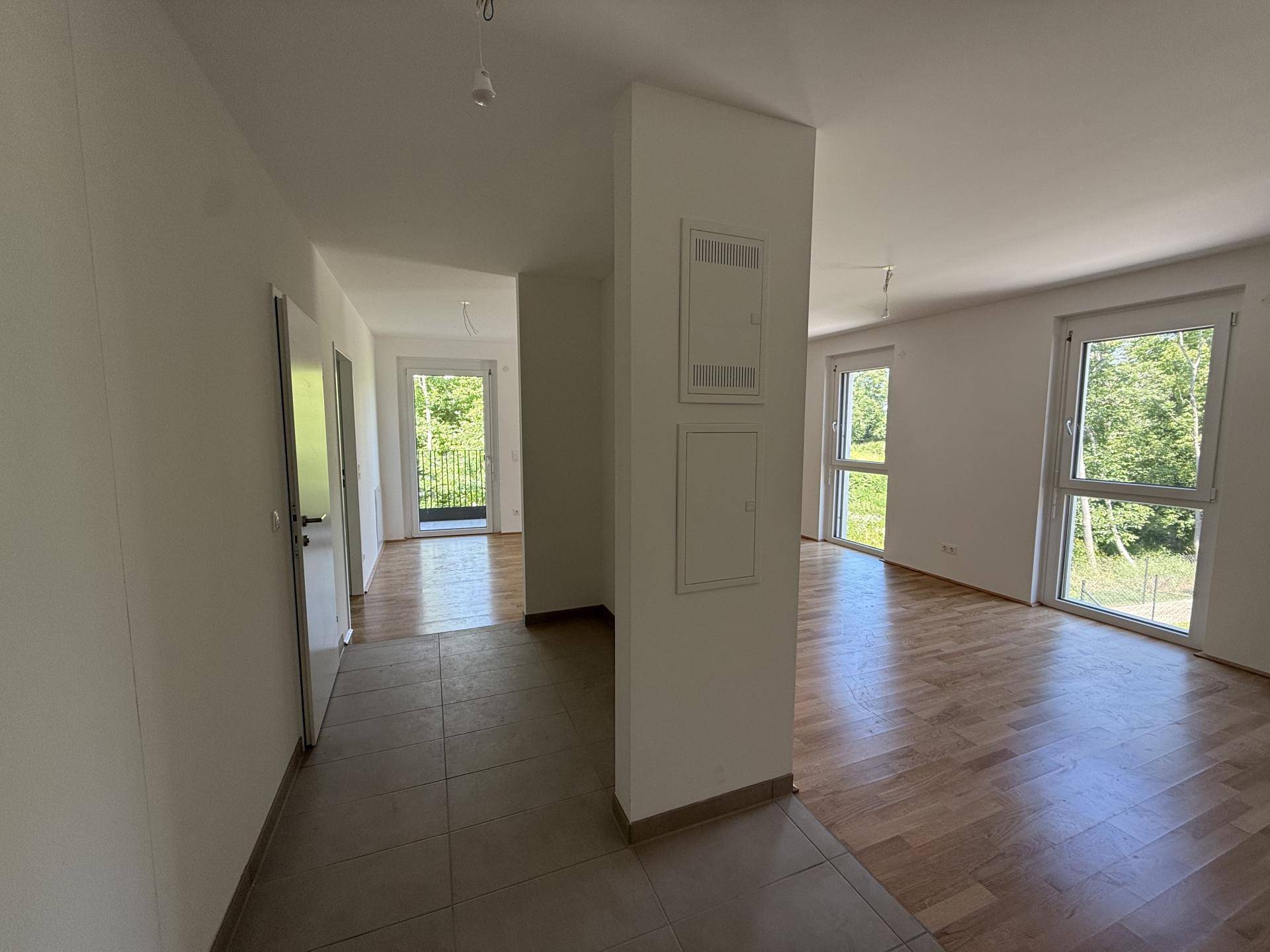Heller Flur mit Fliesenboden, der in einen Wohnbereich mit großen Fenstern und Parkett übergeht.
