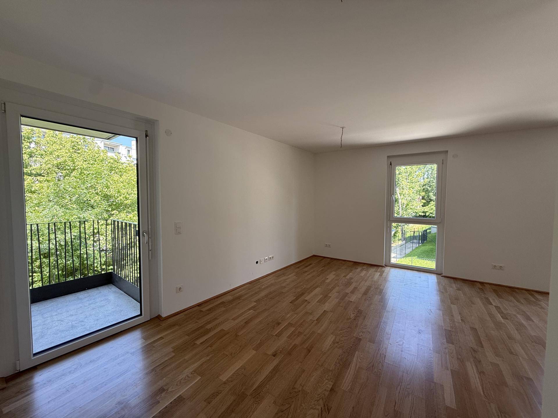 Heller Wohnraum mit Parkettboden und direktem Zugang zu einem Balkon mit Grünblick.