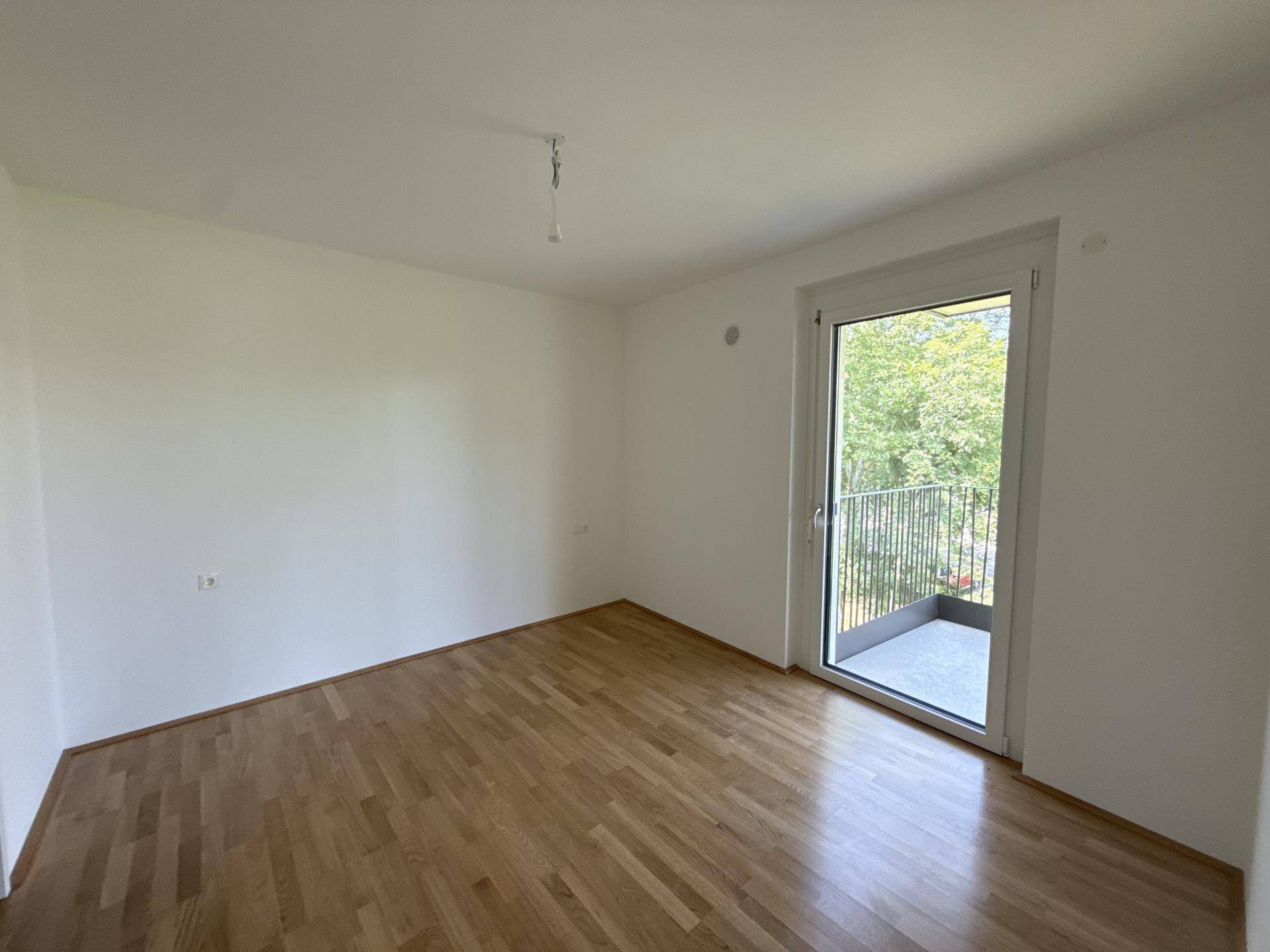 Helles Schlafzimmer mit Parkettboden und direktem Zugang zu einem Balkon.