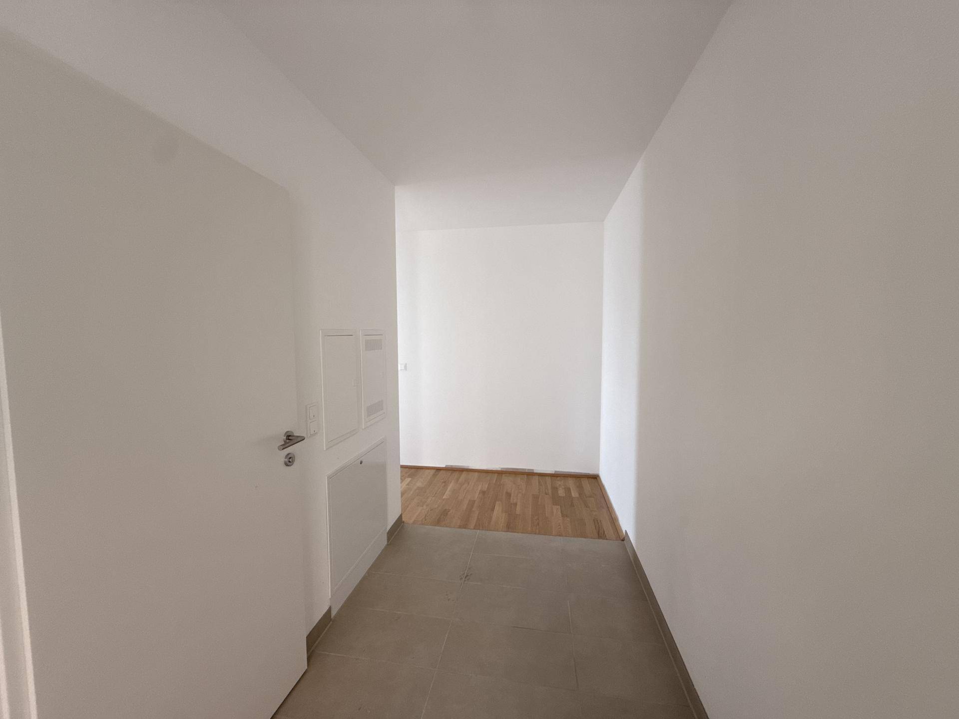 Heller Flur mit Fliesenboden, der in einen Bereich mit Holzparkett übergeht.