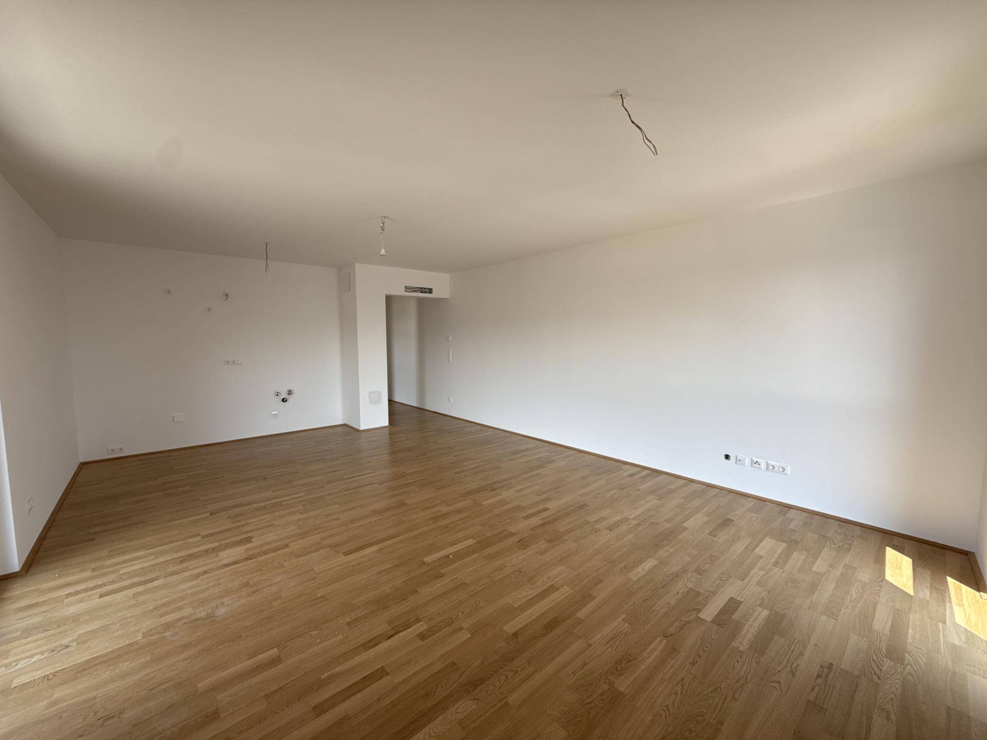 Geräumiges, leeres Wohnzimmer mit hellem Holzparkett und weißen Wänden.