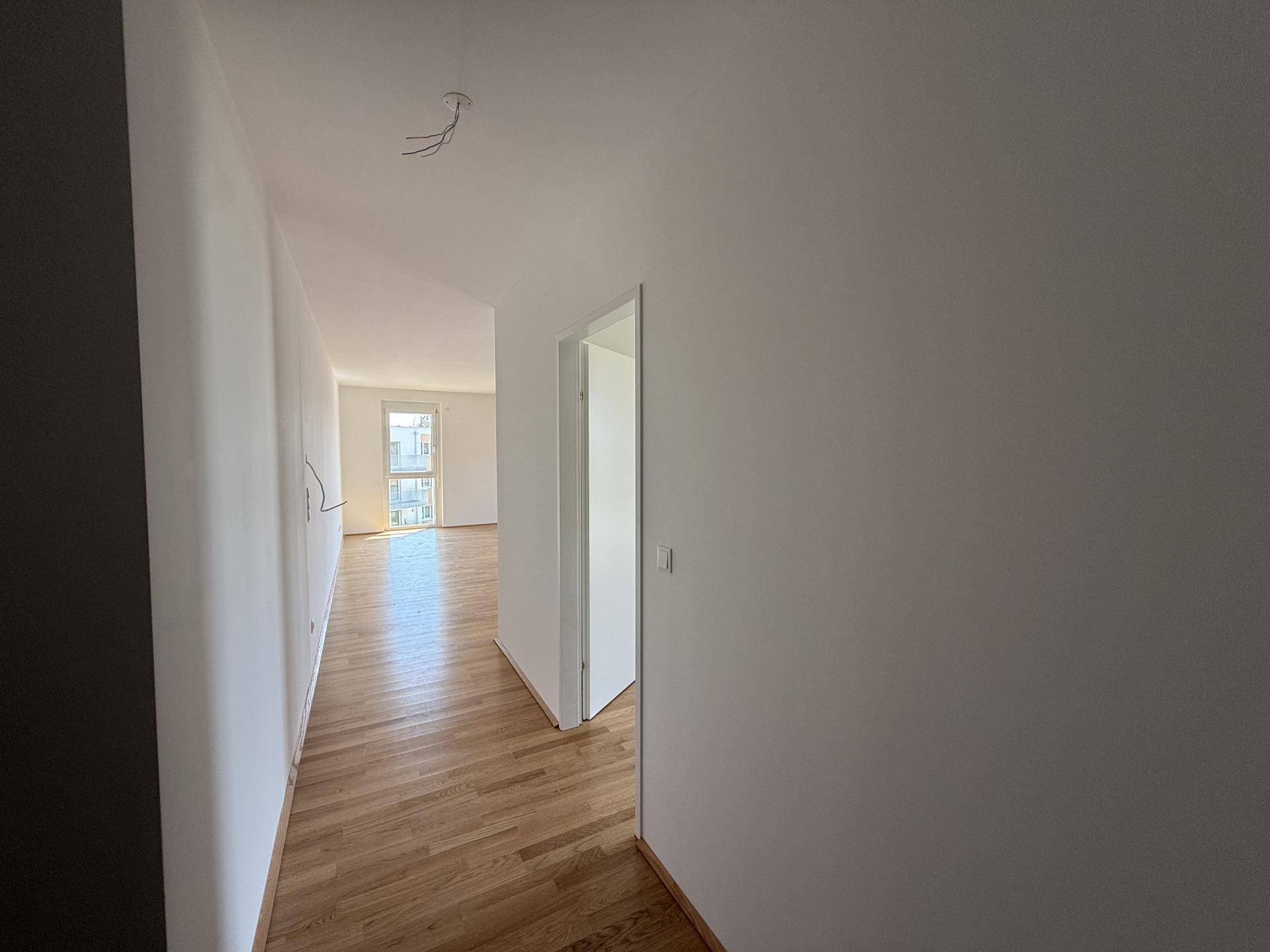 Heller Flur mit Holzboden und weißen Wänden, der zu weiteren Zimmern führt.