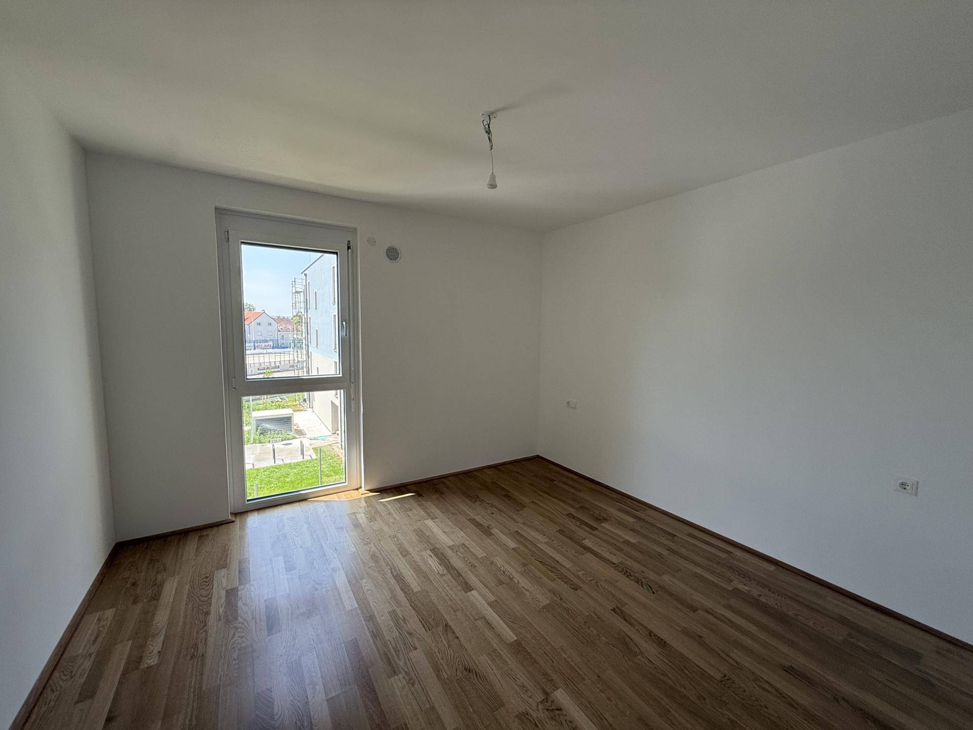 Helles Schlafzimmer mit Holzboden und großem Fenster, das viel Tageslicht hereinlässt.