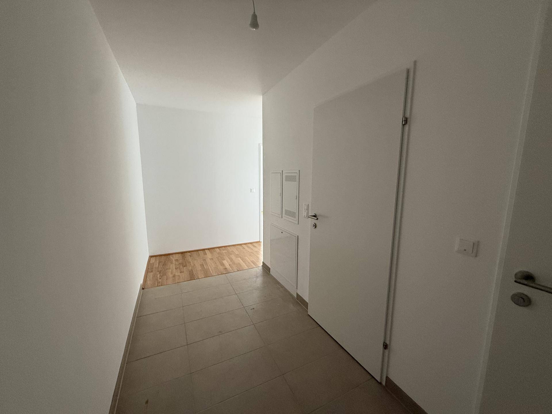 Heller Flur mit Fliesenboden und weißen Wänden, der zu weiteren Räumen führt.