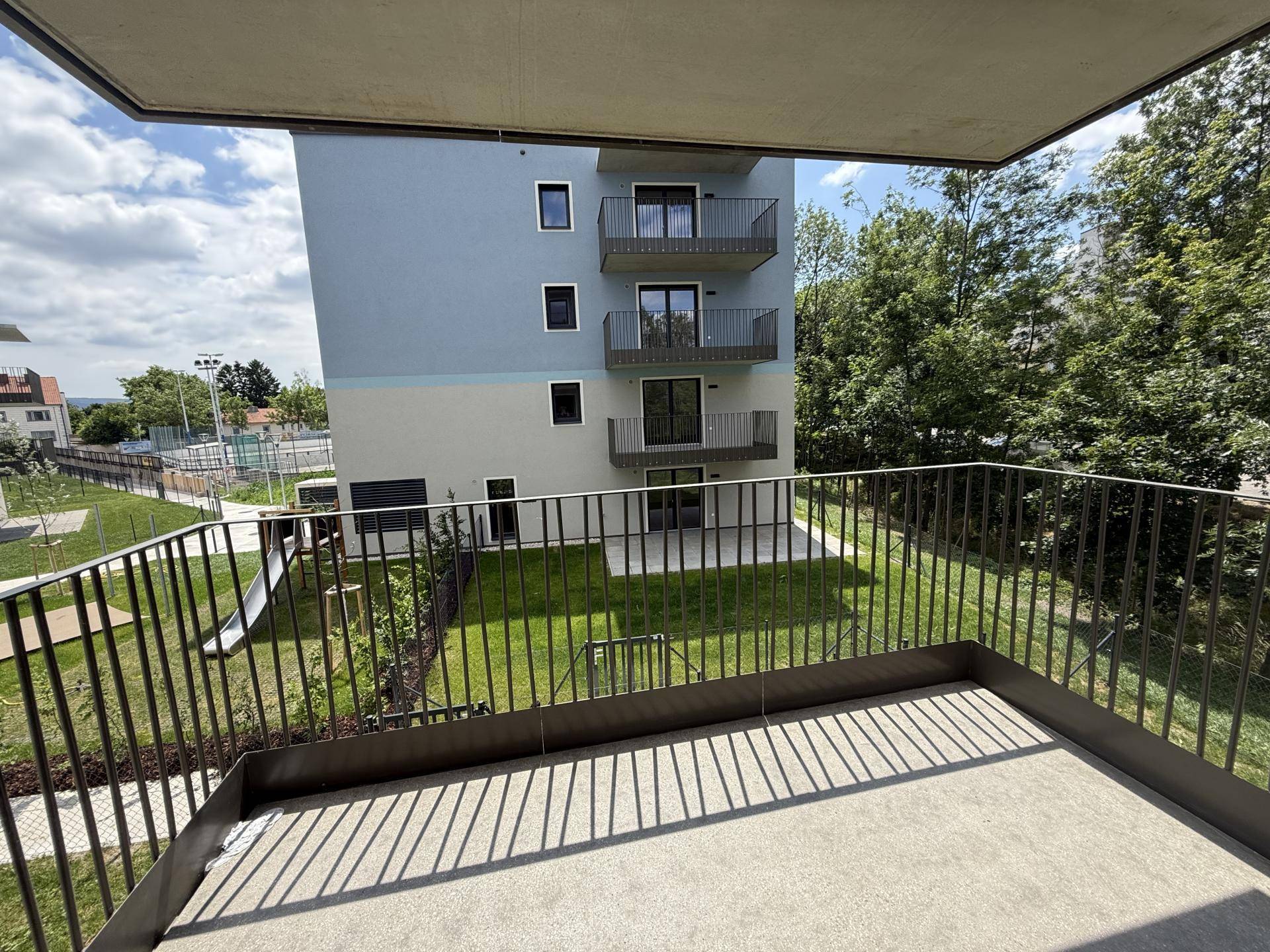 Balkon mit Metallgeländer und Blick auf die umliegende Grünfläche und das moderne Gebäude.