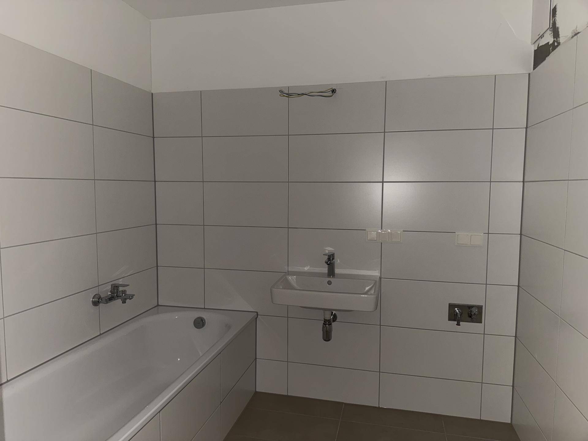 Modernes Badezimmer mit weißen Wandfliesen, Badewanne und Waschbecken, noch ungenutzt.