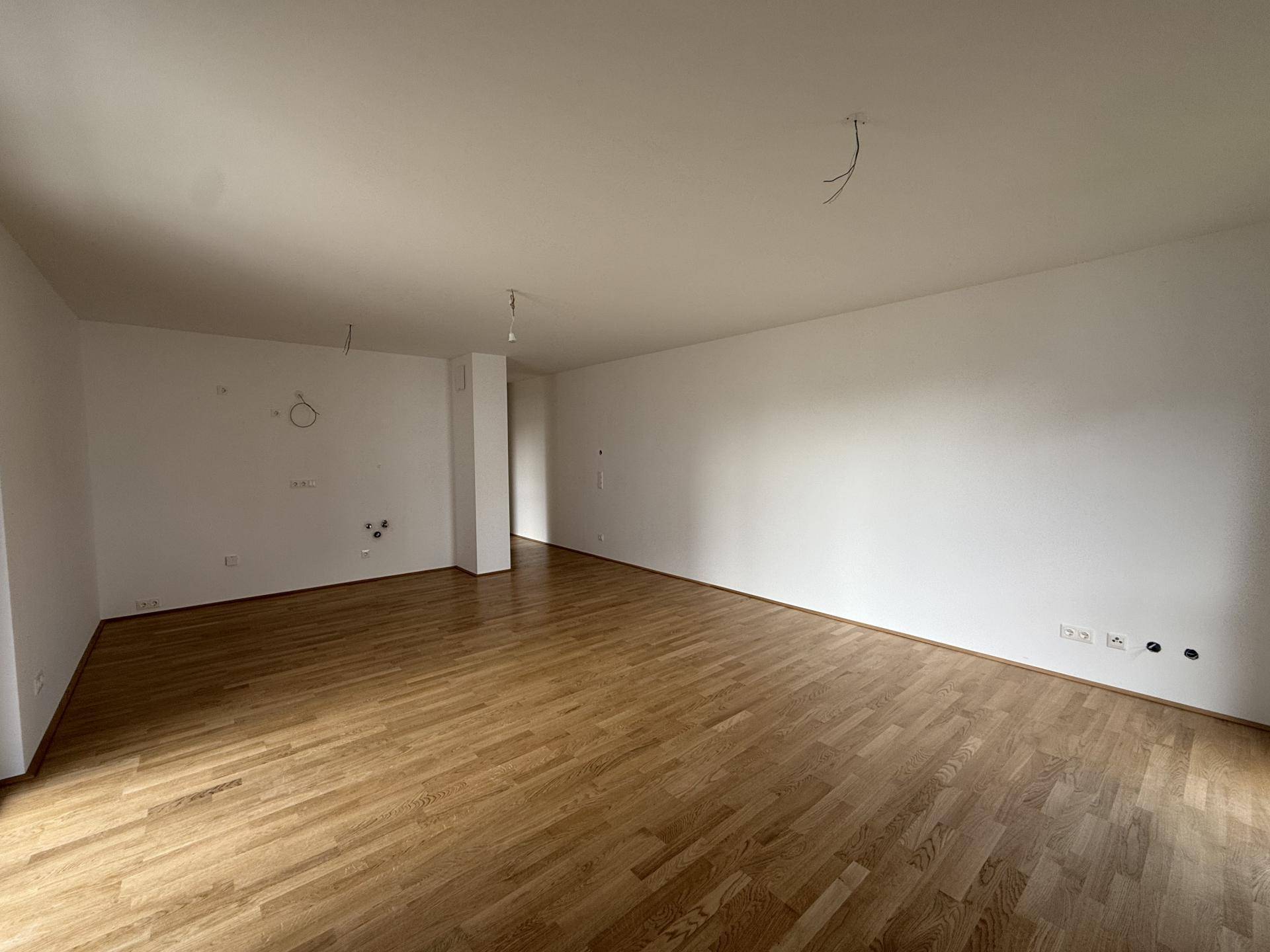 Geräumiges, leeres Wohnzimmer mit hellem Holzparkettboden und weißen Wänden, bereit zum Einzug.
