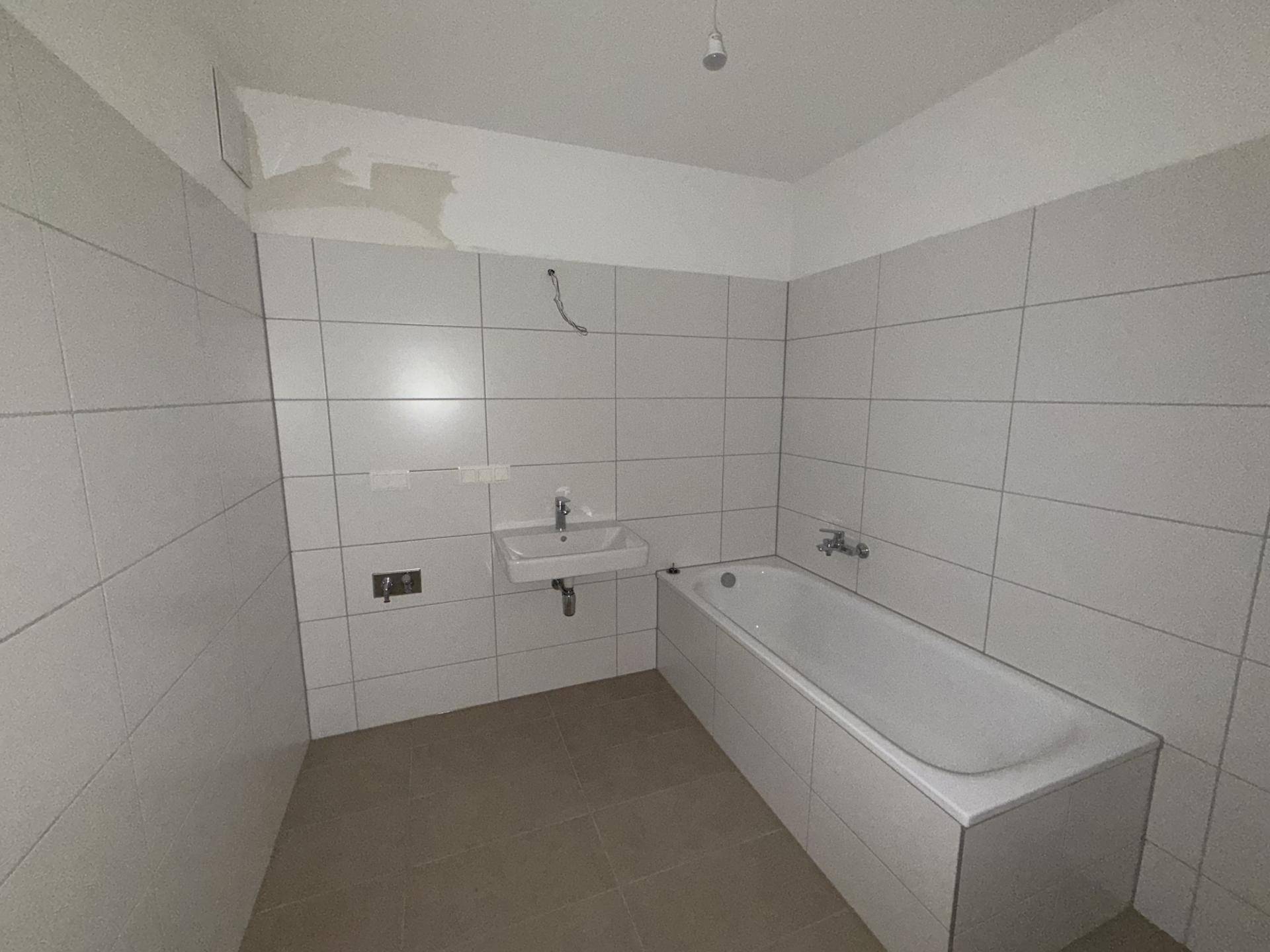Unfertiges Badezimmer mit weißen Wandfliesen, einer Badewanne und einem einzelnen Waschbecken.