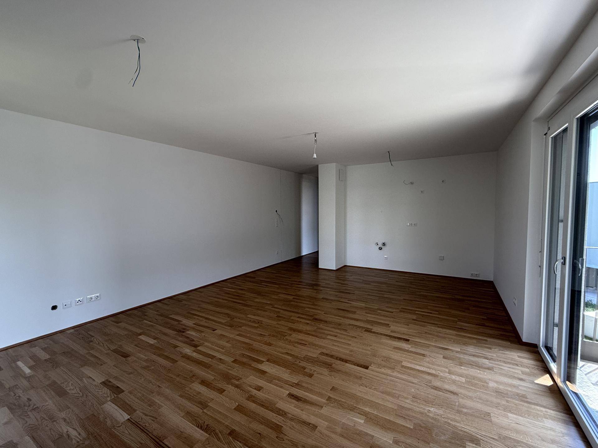 Geräumiges Wohnzimmer mit Holzboden und großem Zugang zu einem Außenbereich.