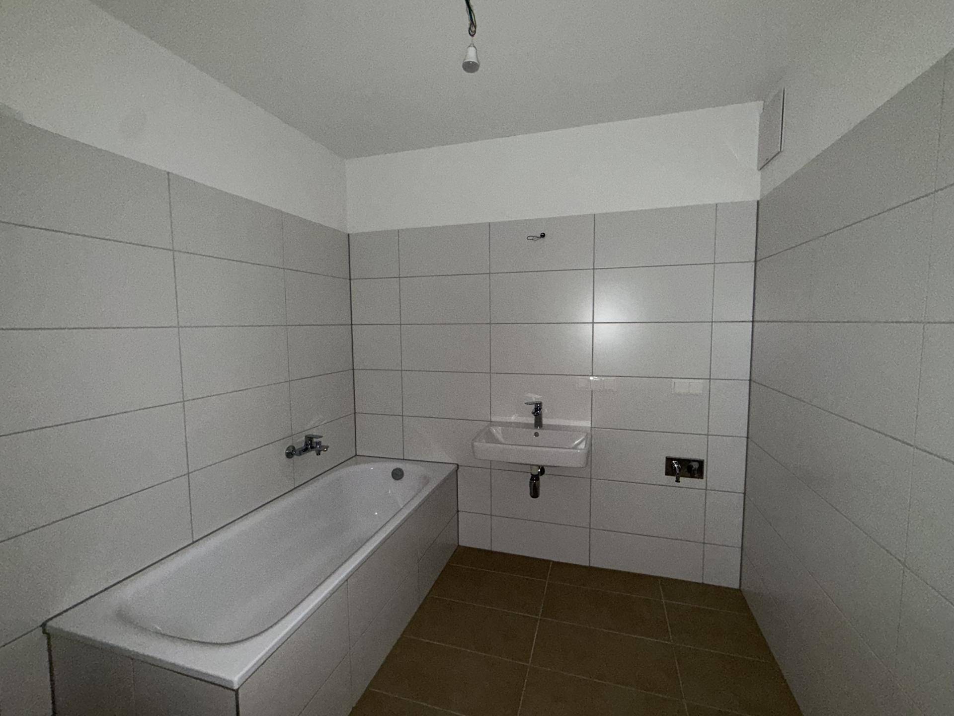 Modern gefliestes Badezimmer mit Badewanne und Waschbecken, bereit für die Endmontage.