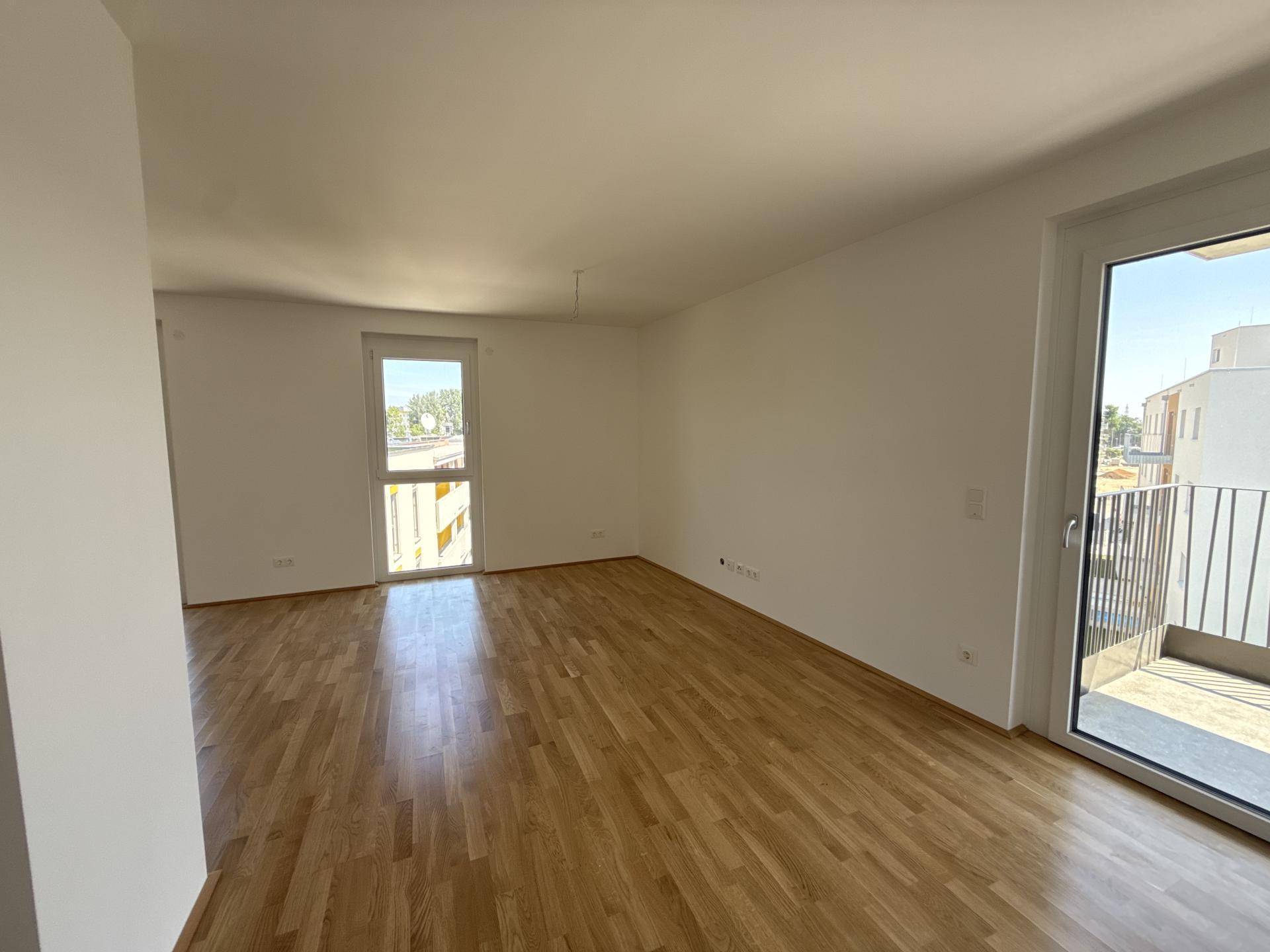 Geräumiges, helles Zimmer mit Holzboden und Zugang zu einem Balkon, ideal für Wohnzwecke.