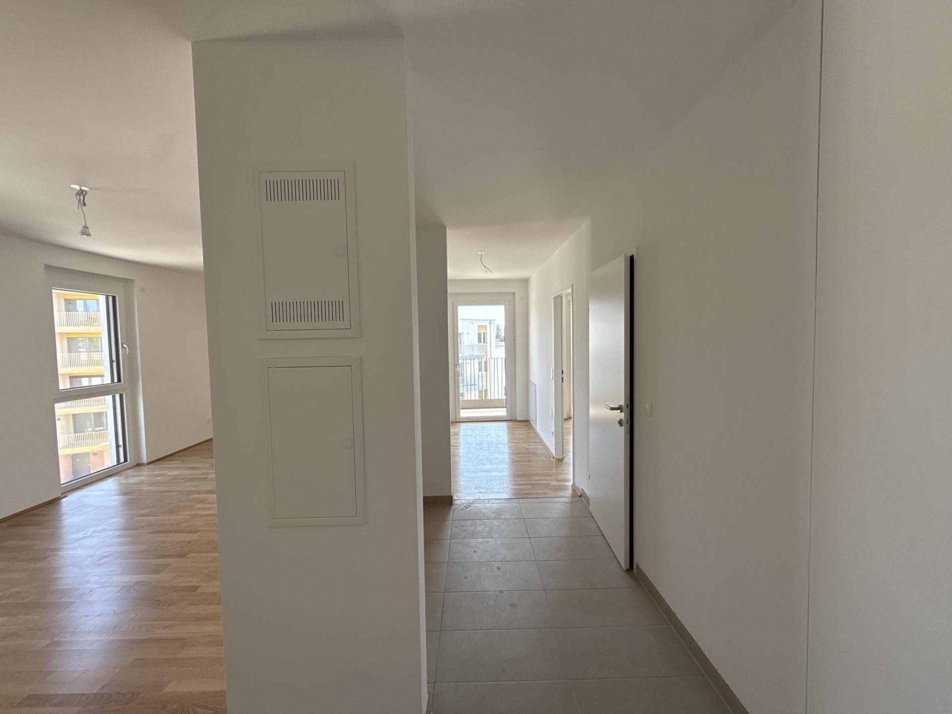 Heller Flur mit Fliesenboden, der zu einem weiteren Raum mit Balkonzugang führt.
