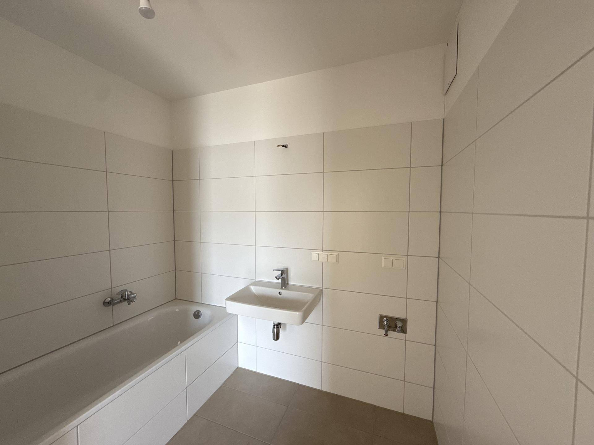 Modernes Badezimmer mit weißen Fliesen, einer Badewanne und einem einzelnen Waschbecken.