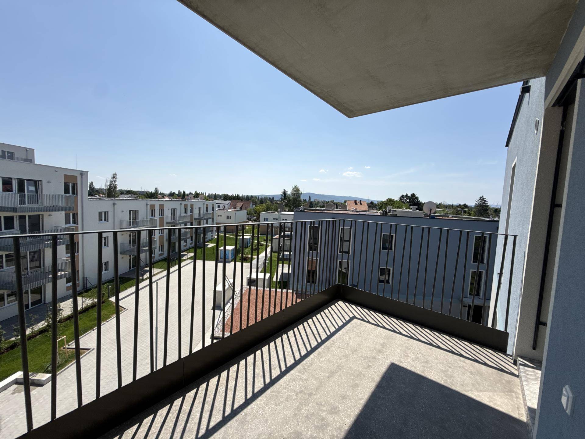 Geräumiger Balkon mit Metallgeländer und weitem Blick über die umliegenden Neubauten und Hügel.