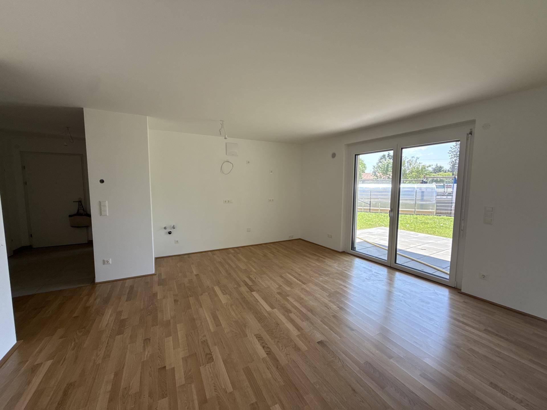 Geräumiges, unmöbliertes Wohnzimmer mit Parkettboden und Zugang zur Terrasse oder zum Garten.