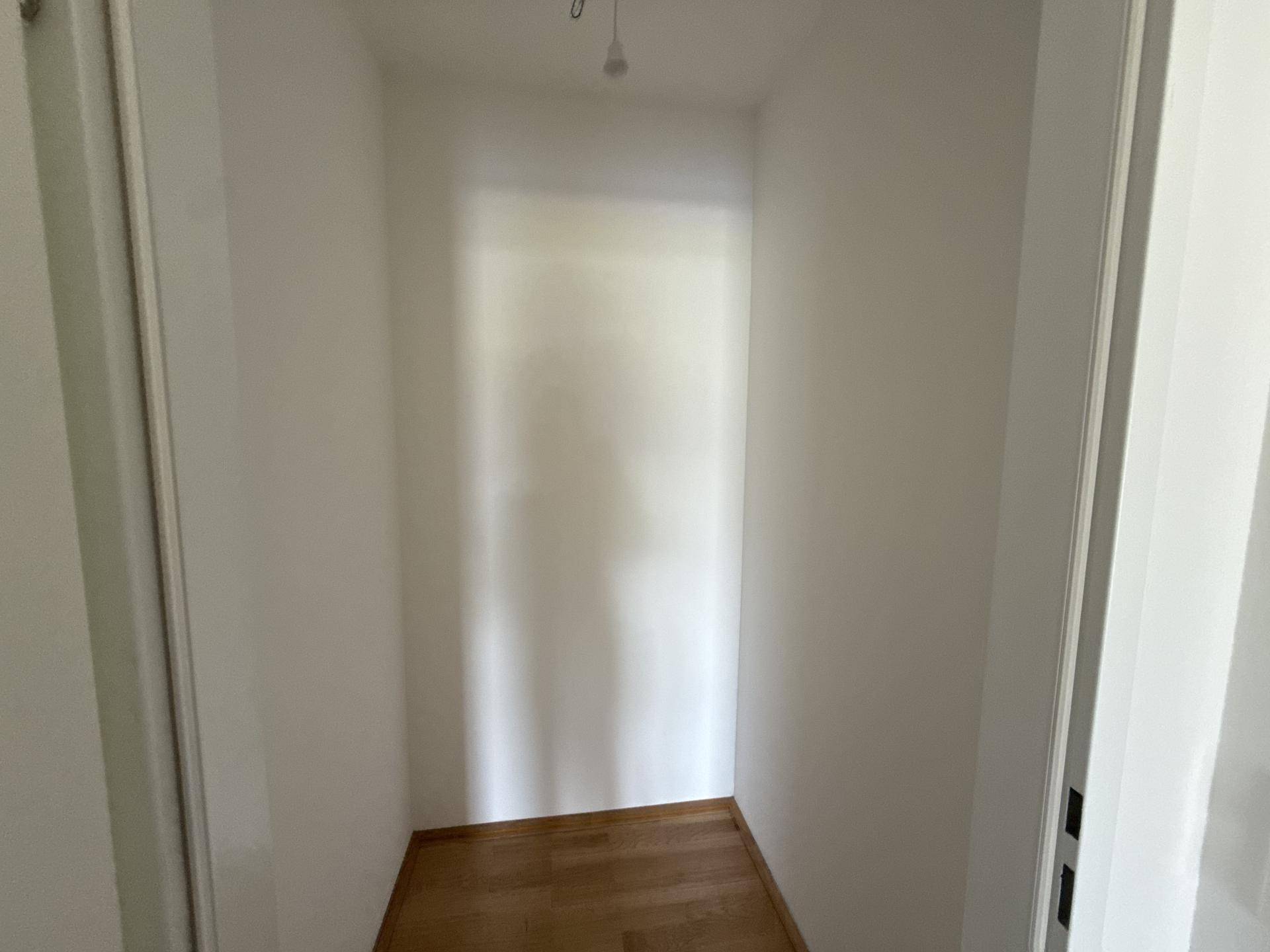 Kleiner, leerer Abstellraum oder begehbarer Kleiderschrank mit Holzboden und weißen Wänden.