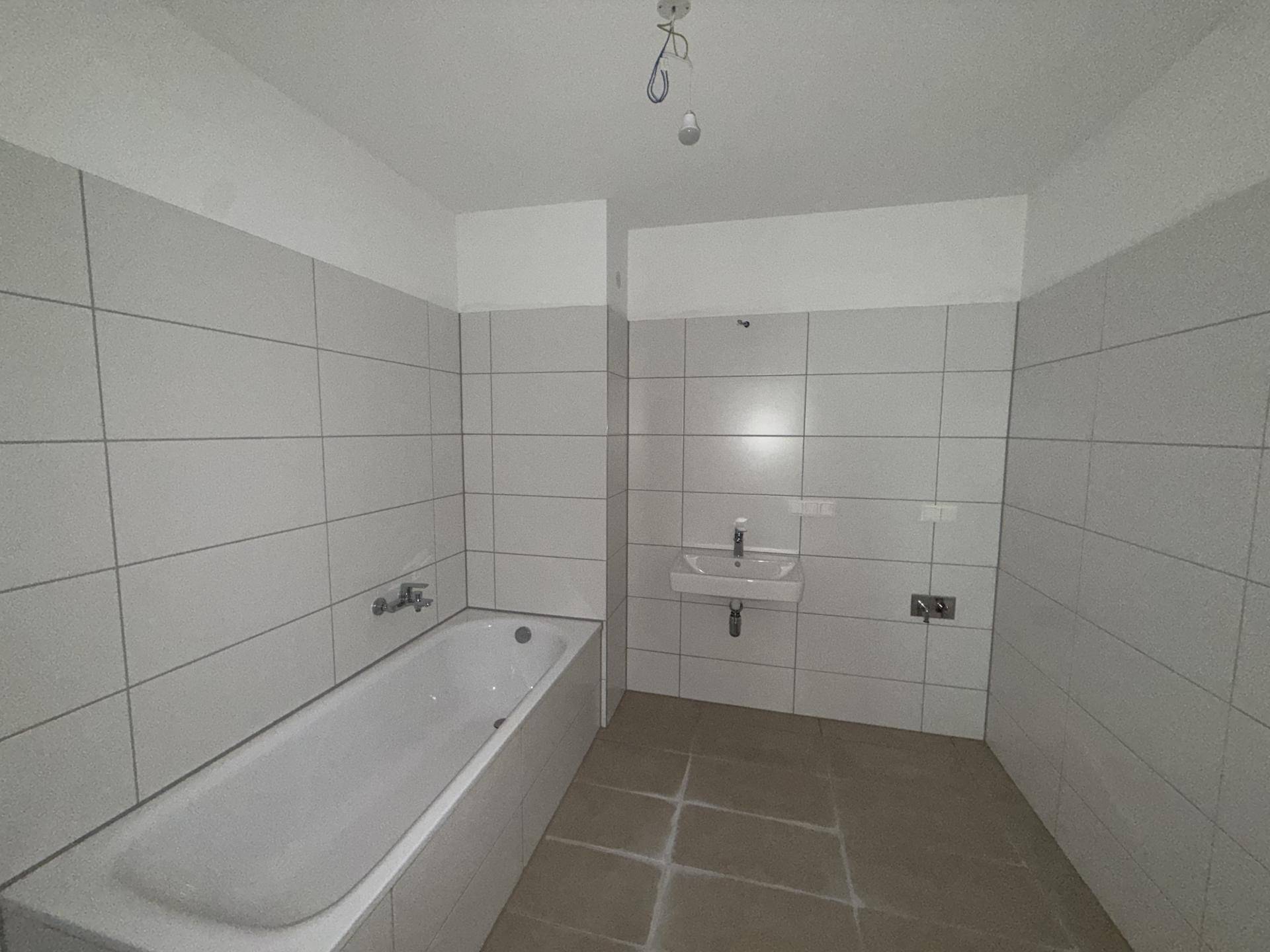 Unfertiges Badezimmer mit Badewanne, Waschbecken und weißen Fliesen an den Wänden.