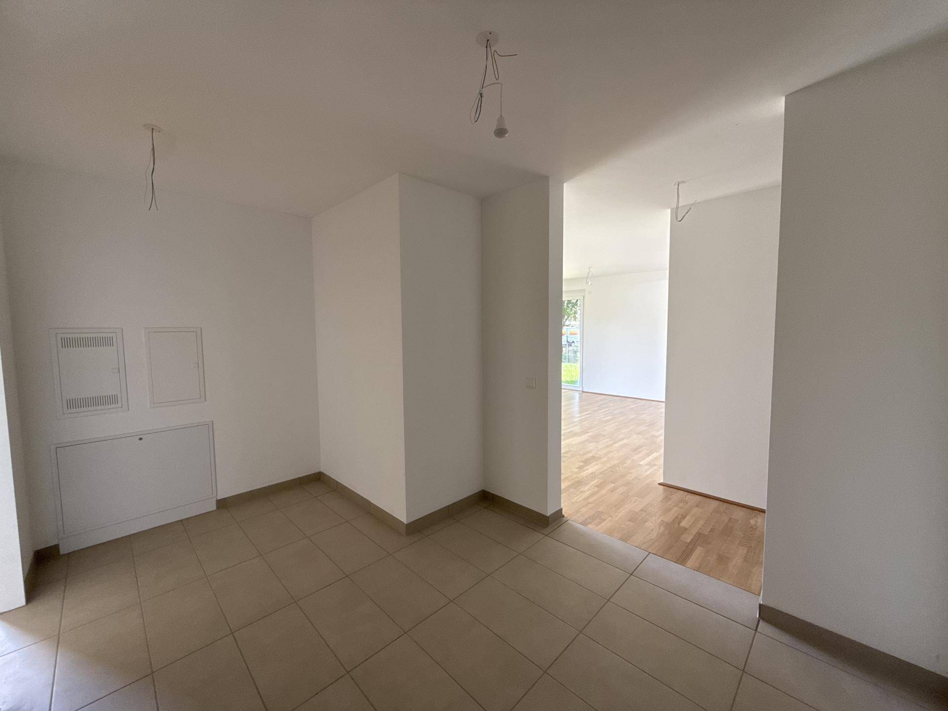 Heller Flurbereich mit Fliesenboden, der zu einem Raum mit Holzboden führt.