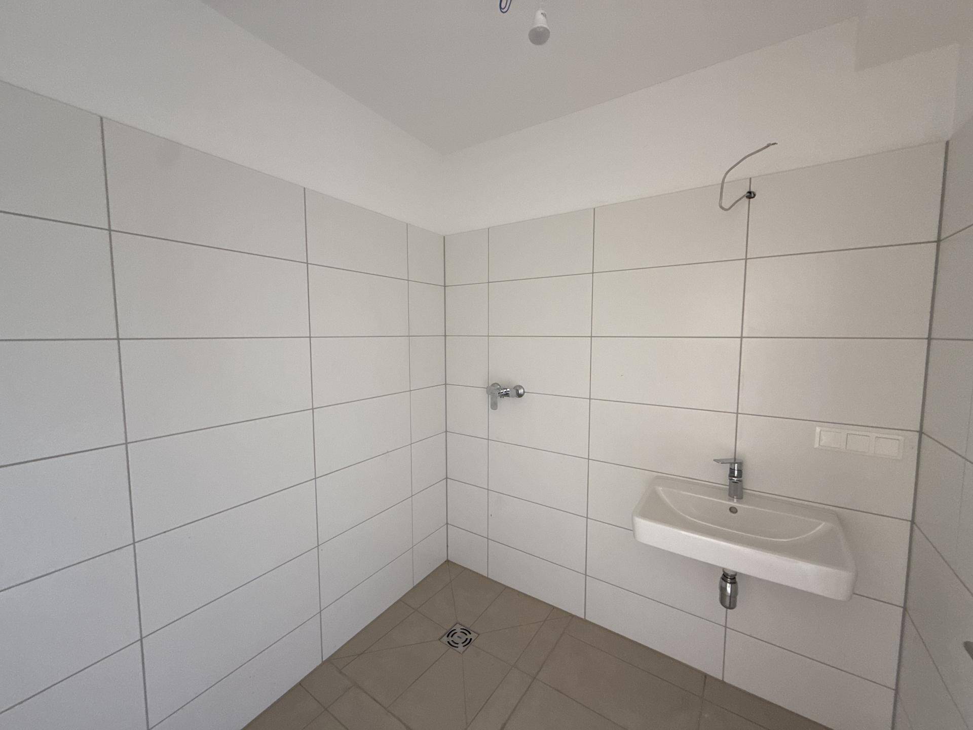 Modernes Badezimmer mit weißen Wandfliesen, Waschbecken und vorbereitetem Duschbereich.