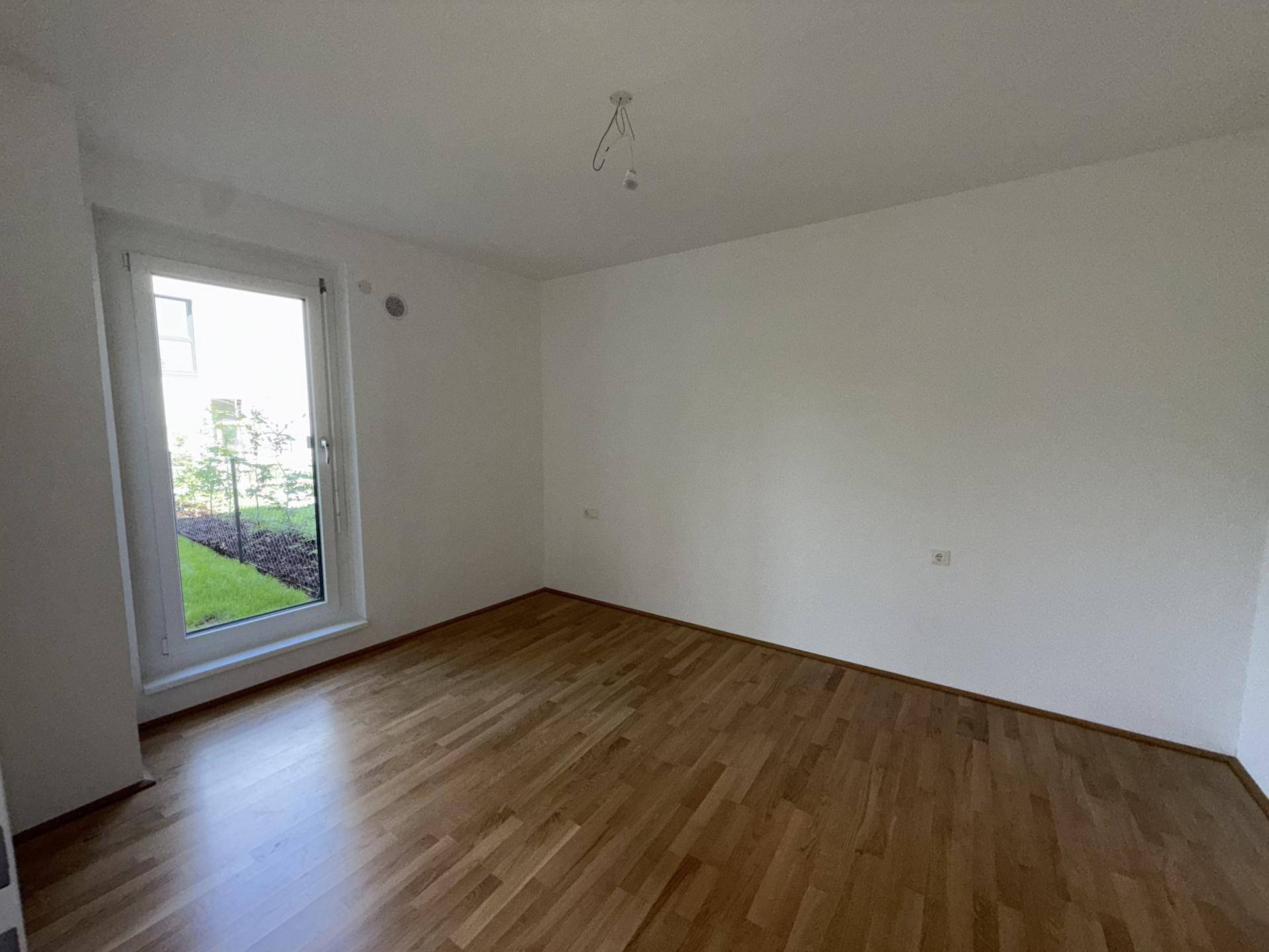 Helles Schlafzimmer mit Holzparkettboden und Zugang zu einem kleinen Außenbereich durch eine Fenstertür.