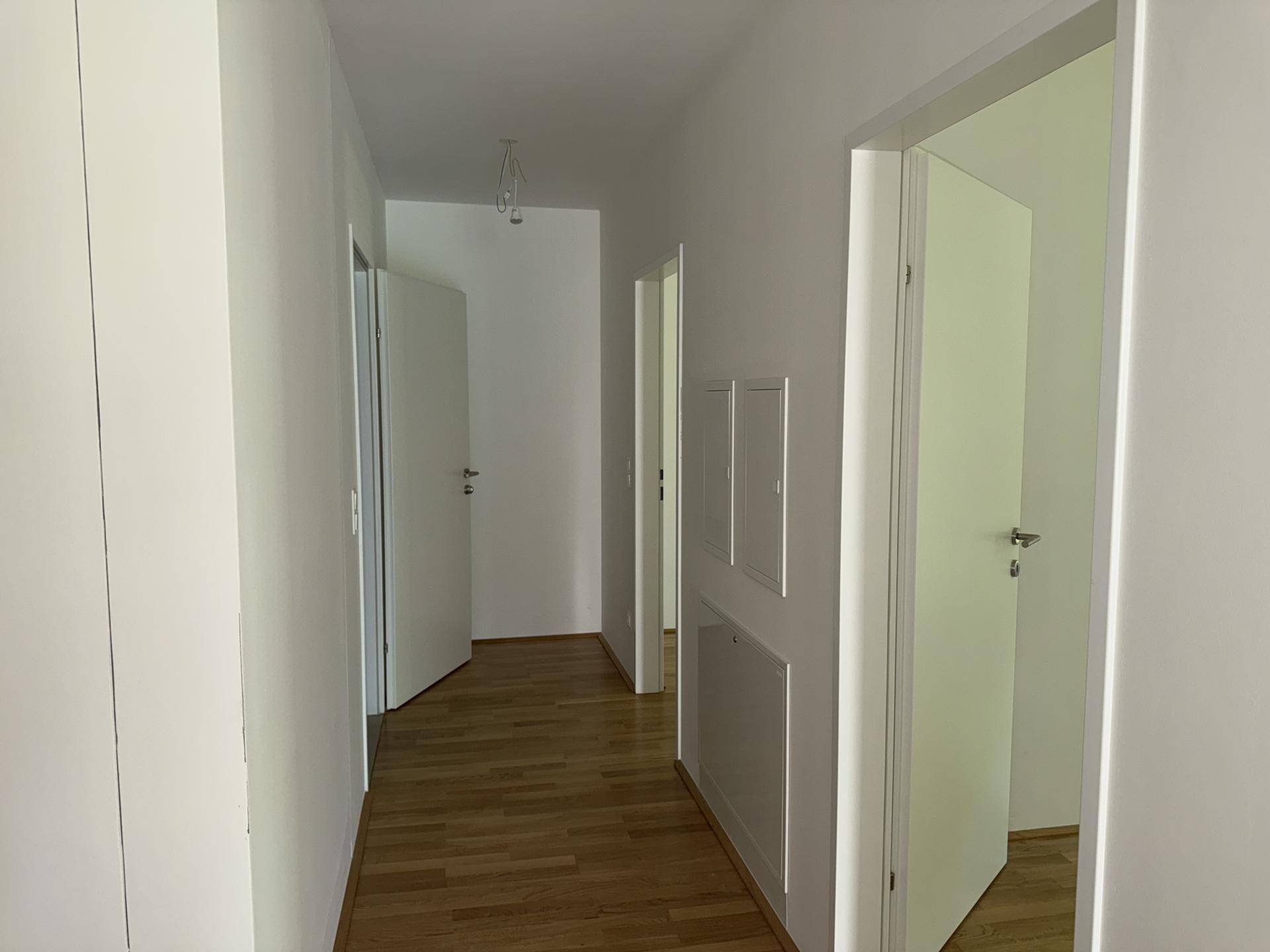 Langer, heller Flur mit Holzparkettboden und mehreren Türen, die zu verschiedenen Räumen führen.