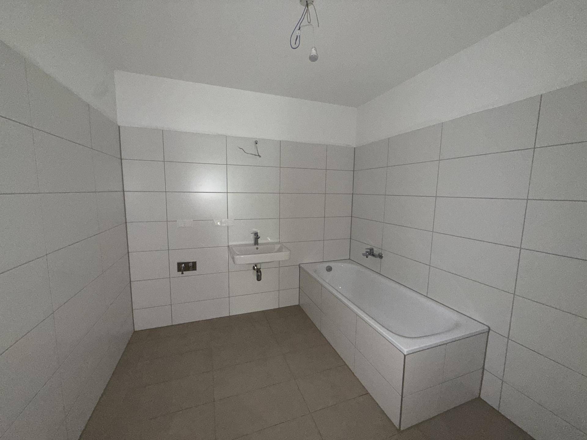 Badezimmer mit weißen Wandfliesen, braunem Boden und einer Badewanne sowie einem einzelnen Waschbecken.