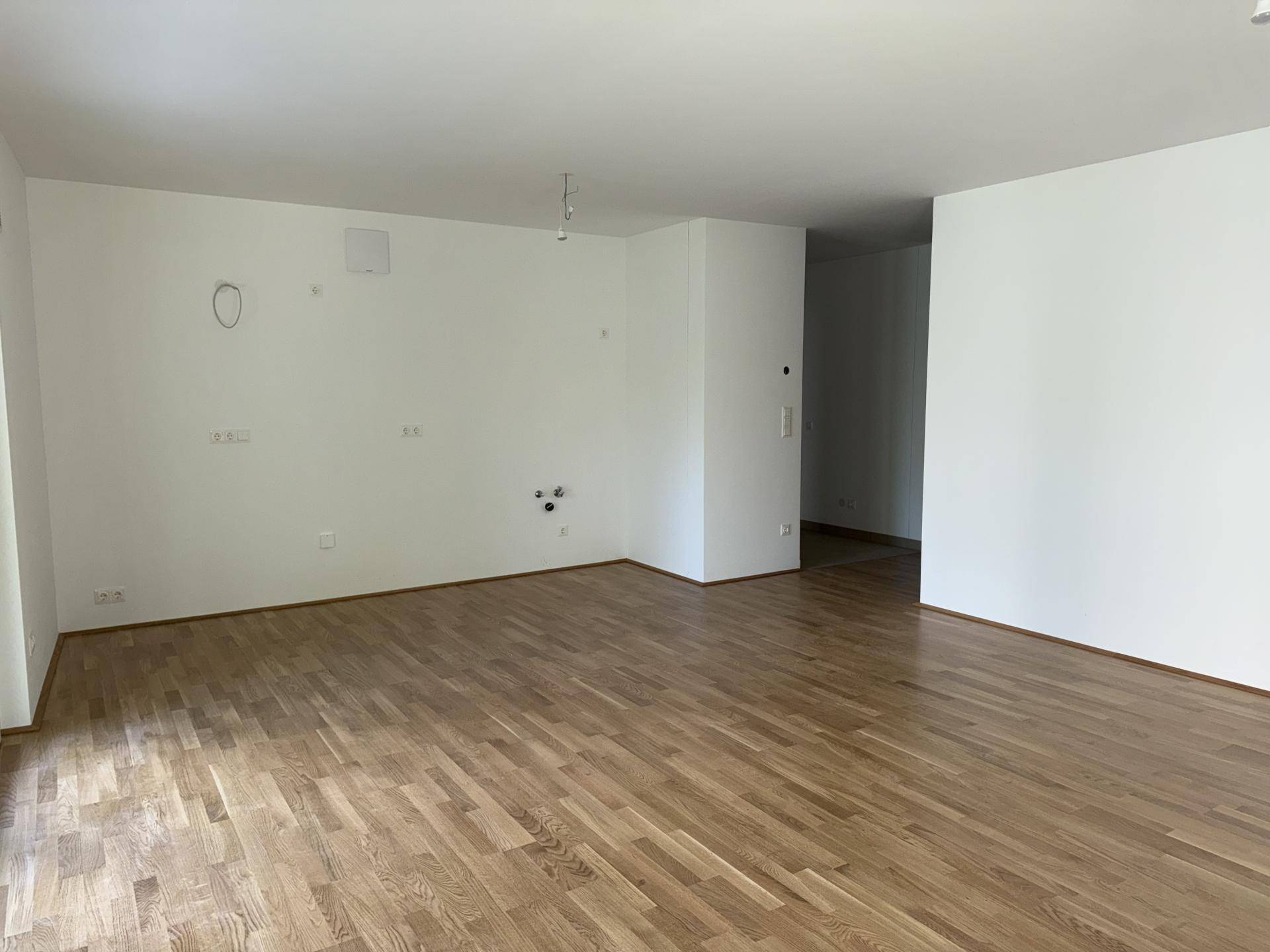 Geräumiges, leeres Wohnzimmer mit hellem Holzparkettboden und weißen Wänden, bereit zur Einrichtung.