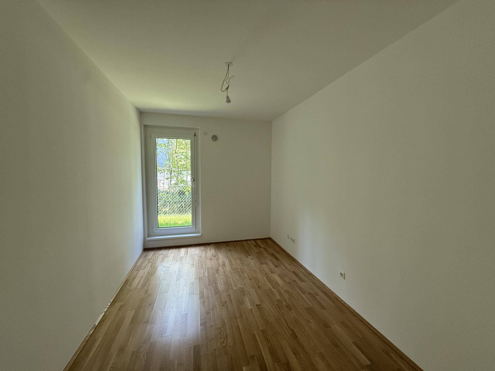 Drittes helles Schlafzimmer mit Holzparkettboden und einer Fenstertür, die viel Tageslicht hereinlässt.