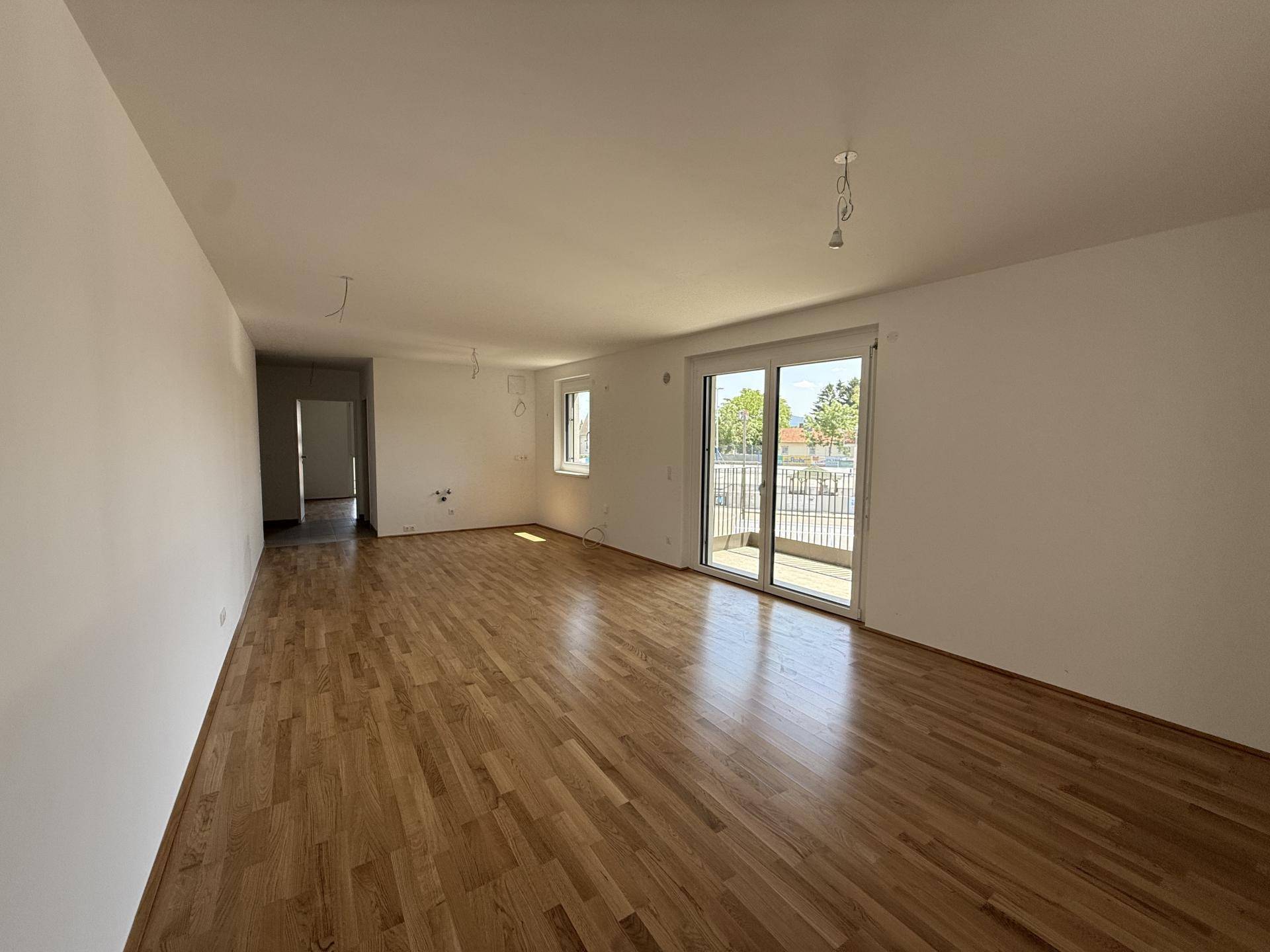 Großzügiges Wohnzimmer mit glänzendem Parkettboden, großen Fenstern und Balkonzugang.