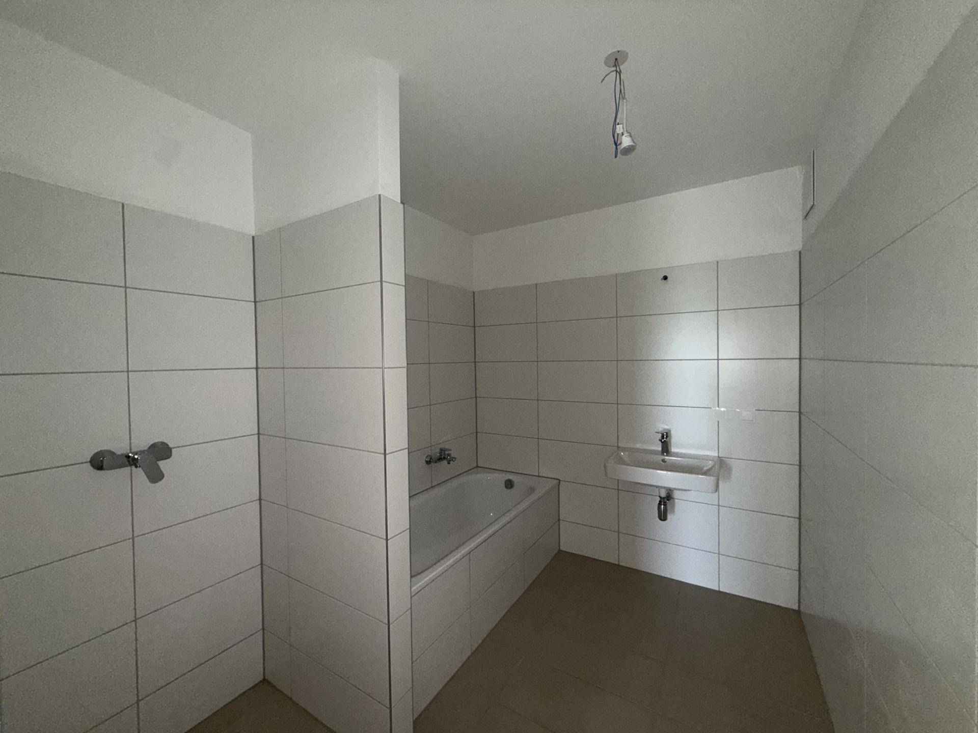 Badezimmer mit Badewanne, Waschbecken und weißen Wand- und Bodenfliesen in schlichtem Design.