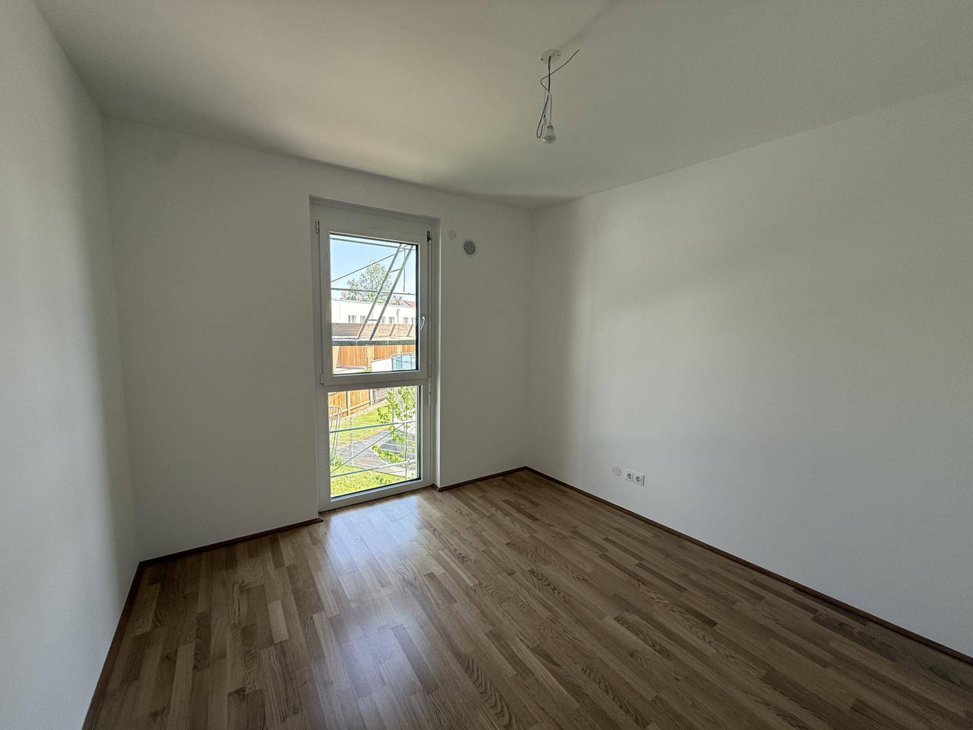 Helles Zimmer mit Parkettboden und großem Fenster, ideal als Schlaf- oder Arbeitszimmer.