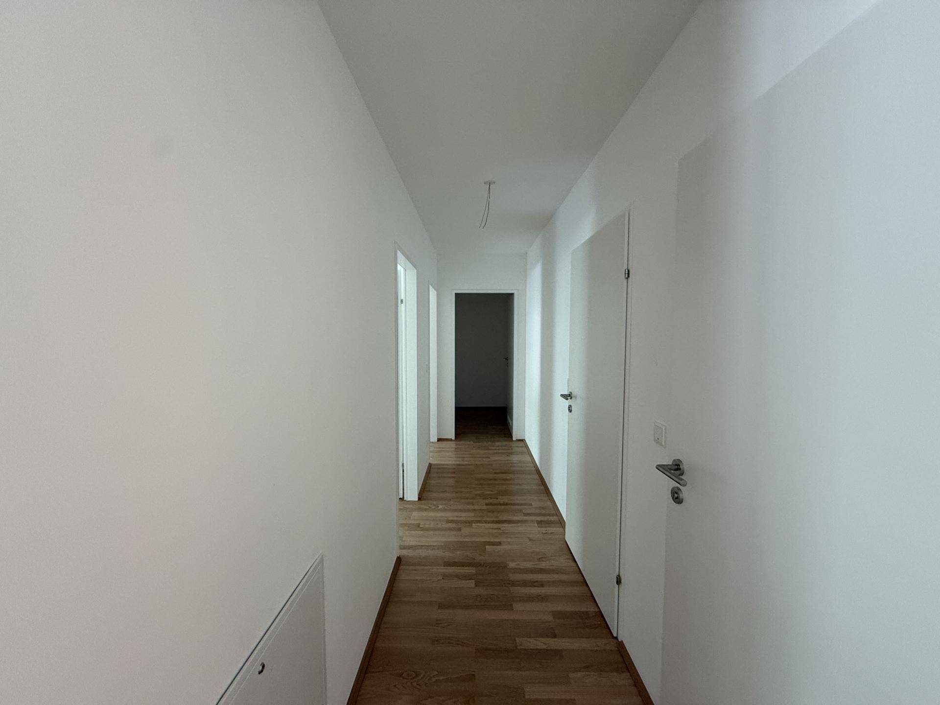 Langer, heller Flur mit Holzboden und weißen Wänden, der zu weiteren Zimmern führt.