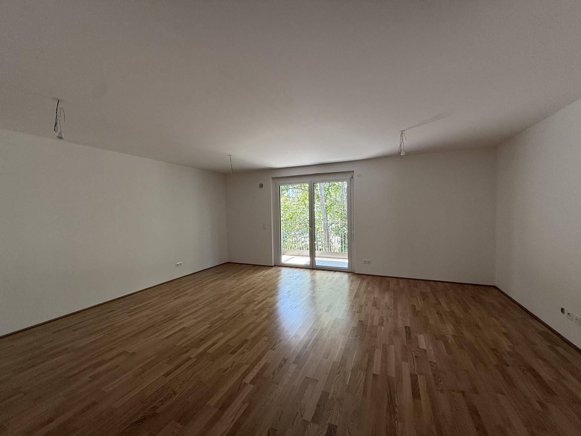 Helles und geräumiges Wohnzimmer mit Holzboden und Zugang zu einem Balkon.