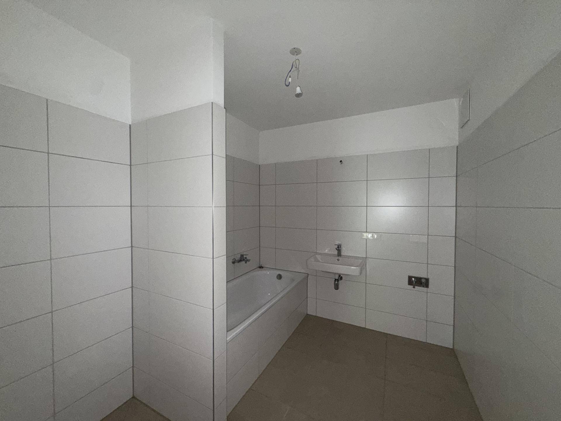 Badezimmer mit Badewanne, Waschbecken und hellen Fliesen, bereit für die Endmontage der Armaturen.