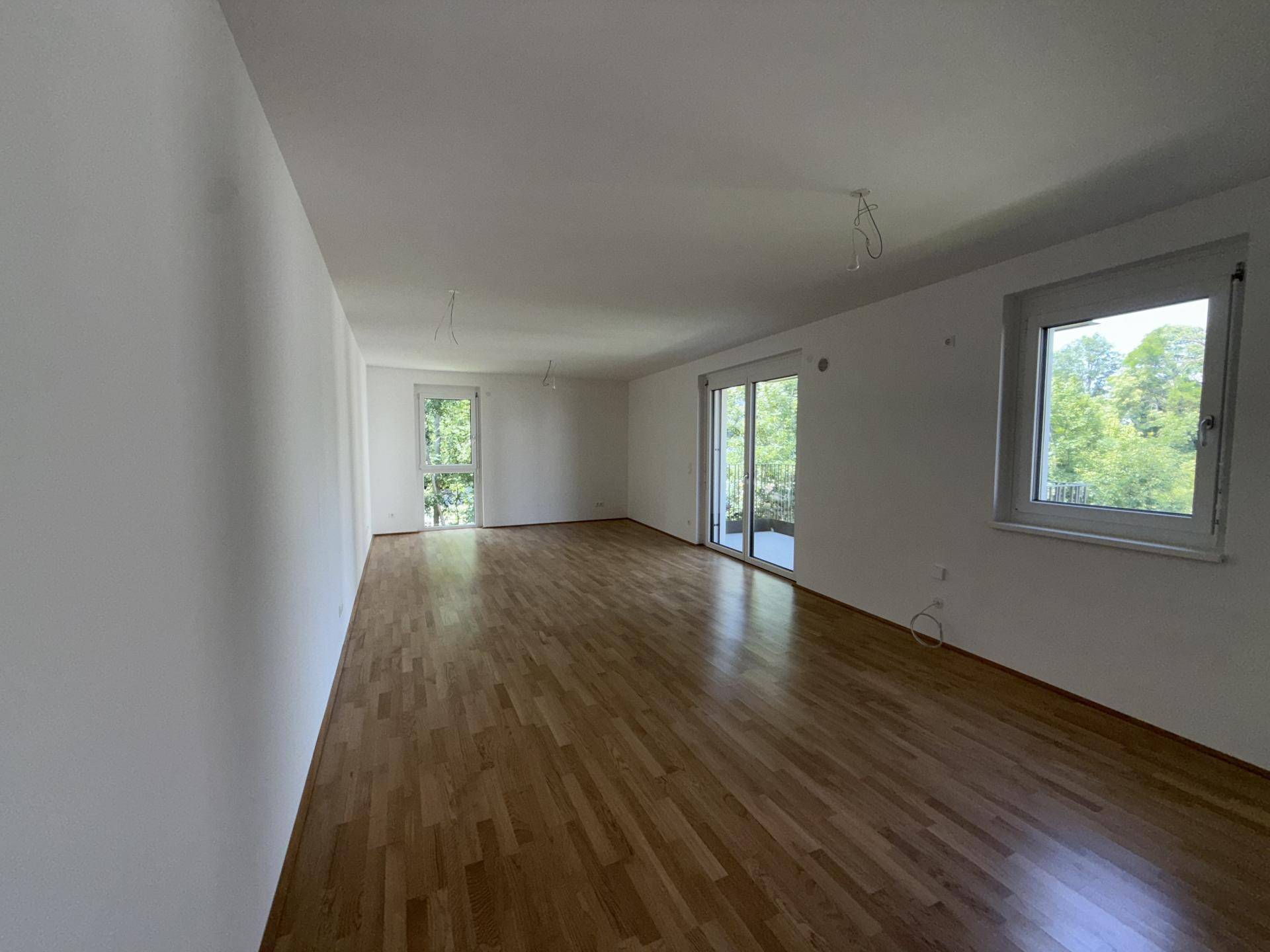 Geräumiges Wohnzimmer mit Parkettboden, großen Fenstern und direktem Balkonzugang mit Grünblick.