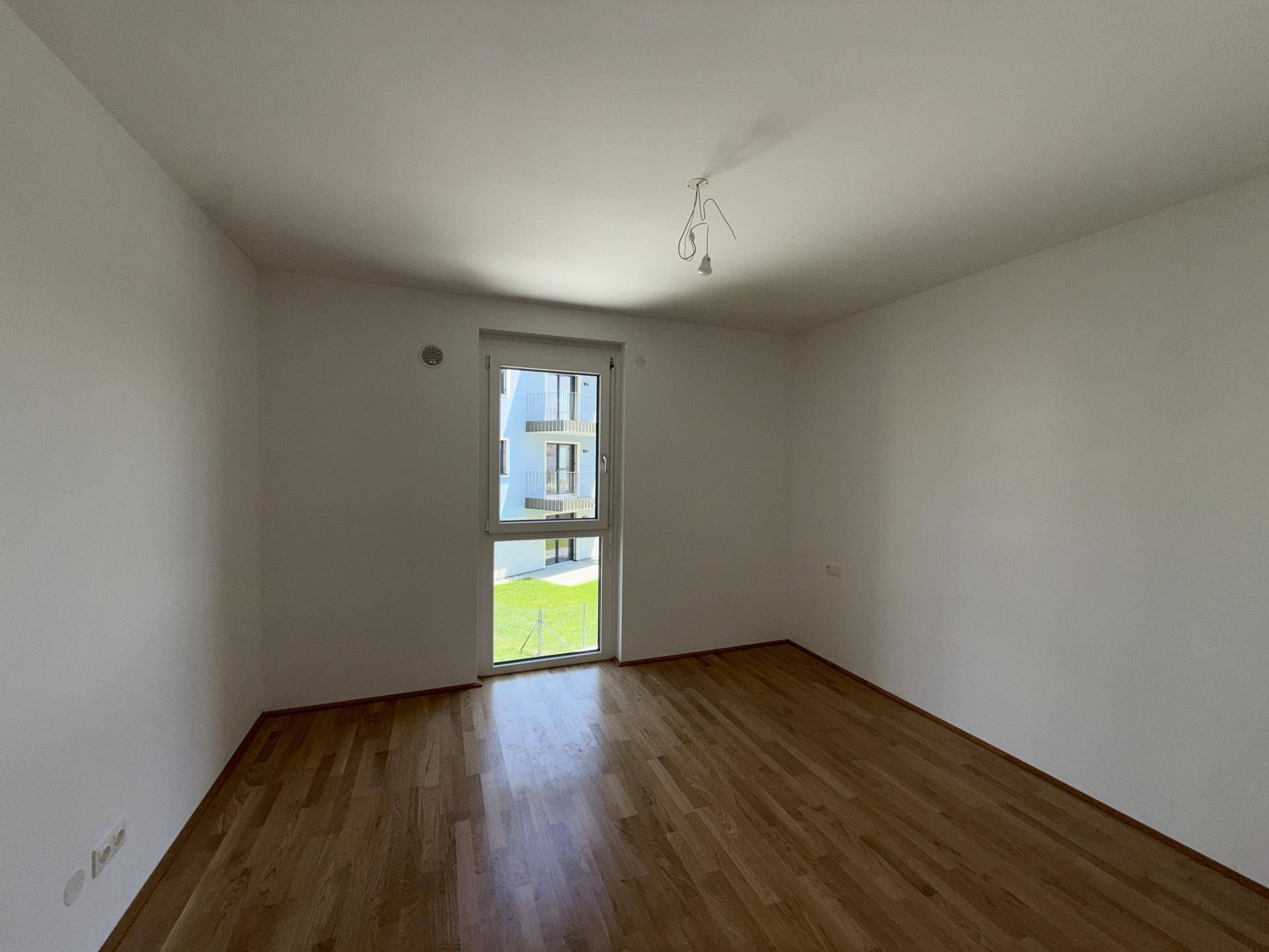 Schlafzimmer mit Parkettboden und bodentiefem Fenster, das einen angenehmen Blick ins Grüne bietet.