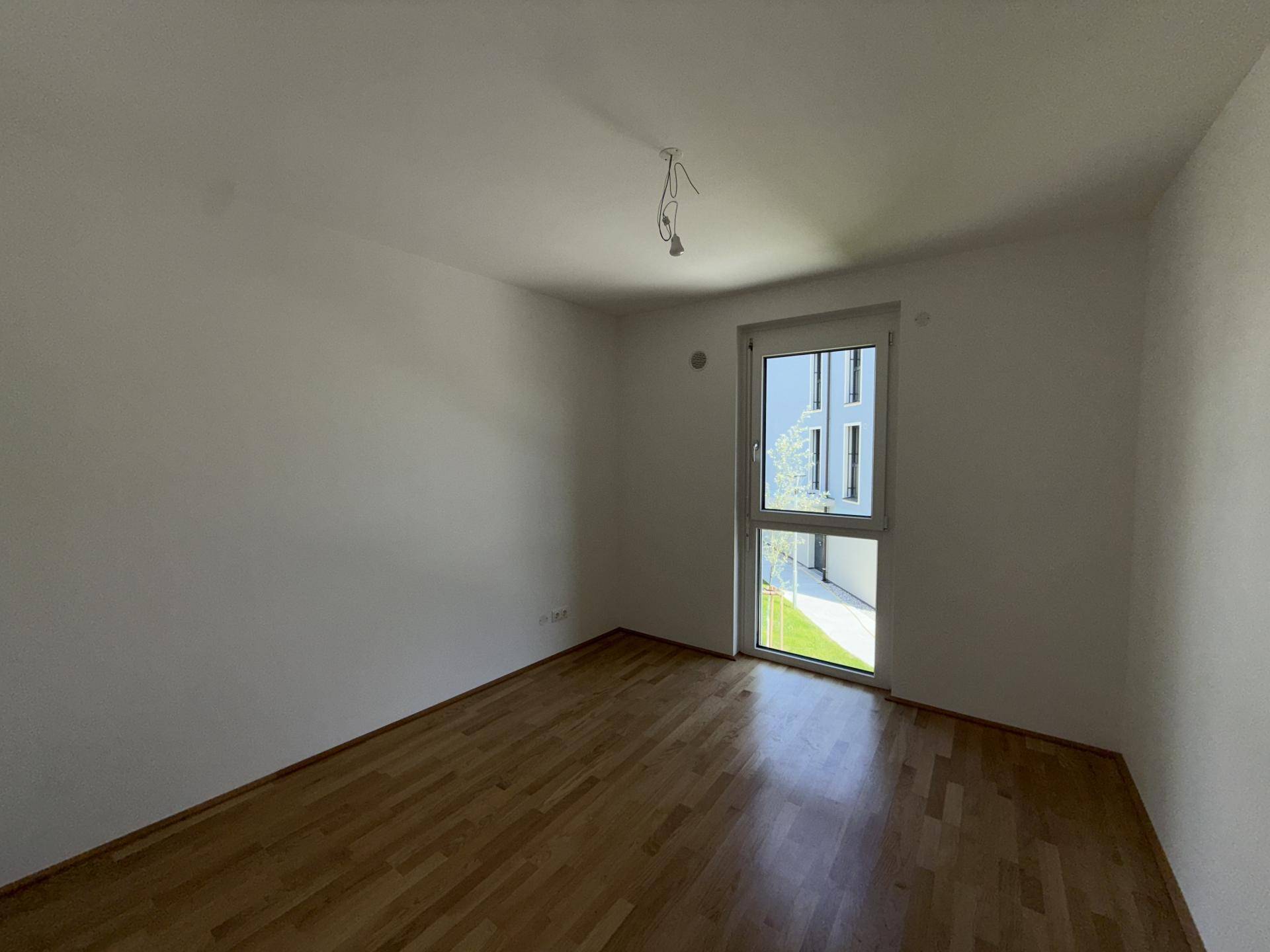 Helles Schlafzimmer mit Parkettboden und Fenster, das einen Blick auf den Innenhof ermöglicht.