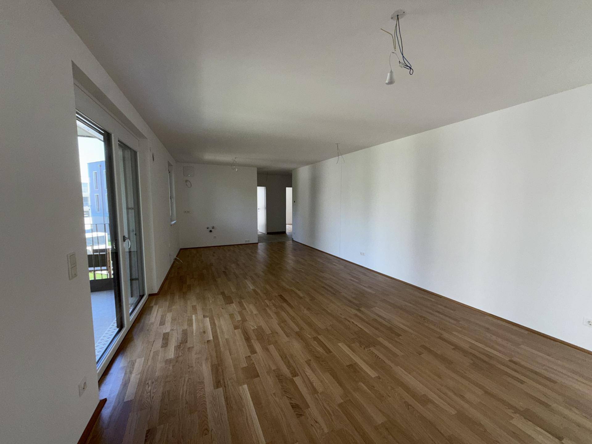 Lichterfüllter Wohnbereich mit Holzparkett, großen Fenstern und Zugang zu einem Außenbereich.