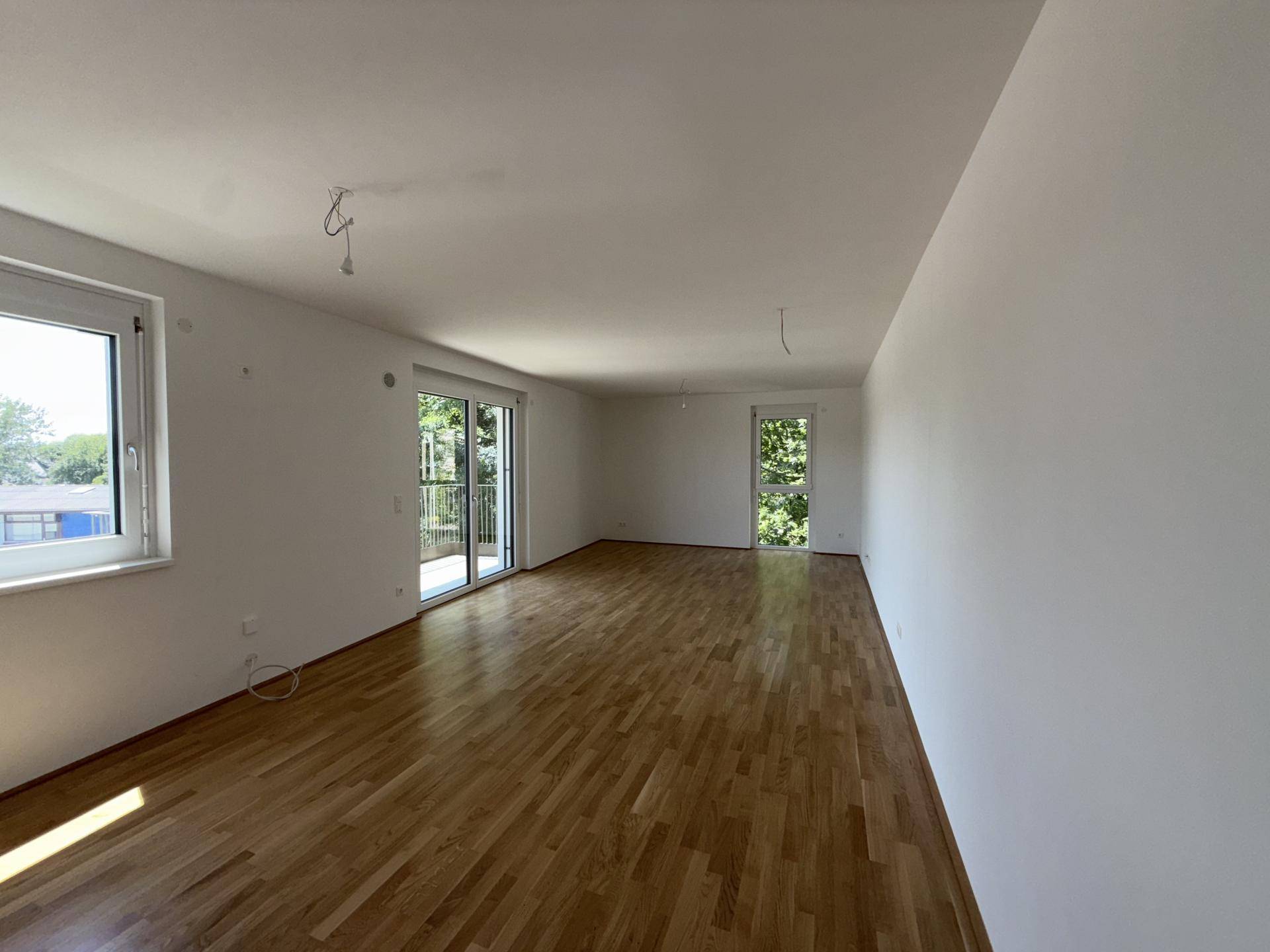 Lichtdurchflutetes Wohnzimmer mit Holzboden, großen Fenstern und Zugang zum Außenbereich.