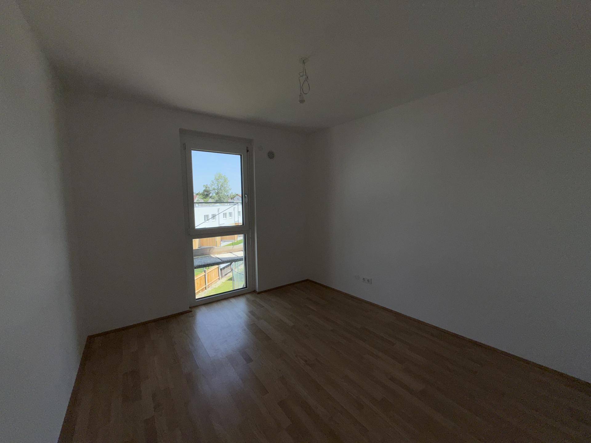 Leeres Zimmer mit Holzboden und einem großen Fenster, ideal als Schlaf- oder Arbeitszimmer.