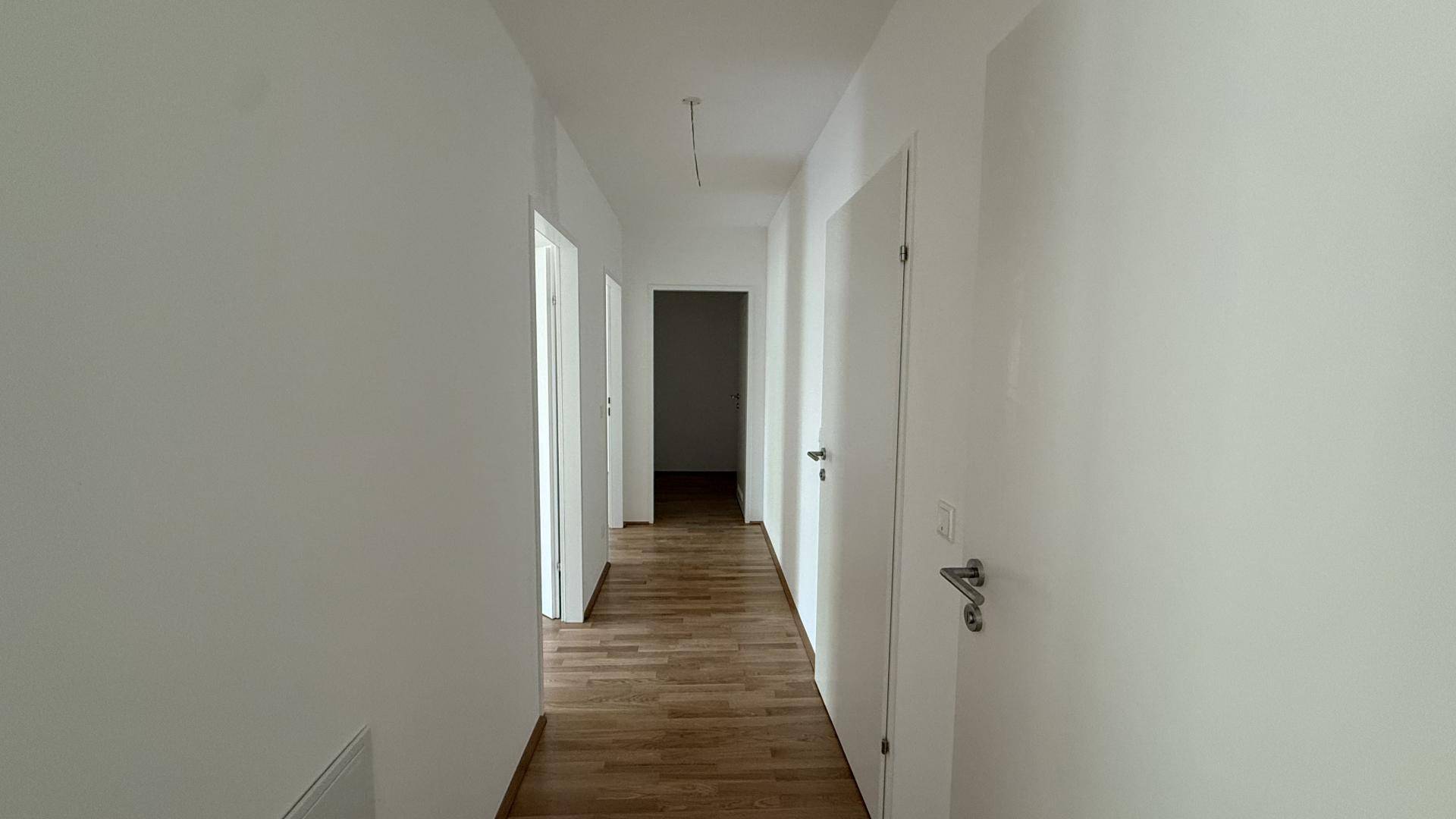 Langer, heller Flur mit Holzboden und weißen Wänden, der zu verschiedenen Zimmern führt.