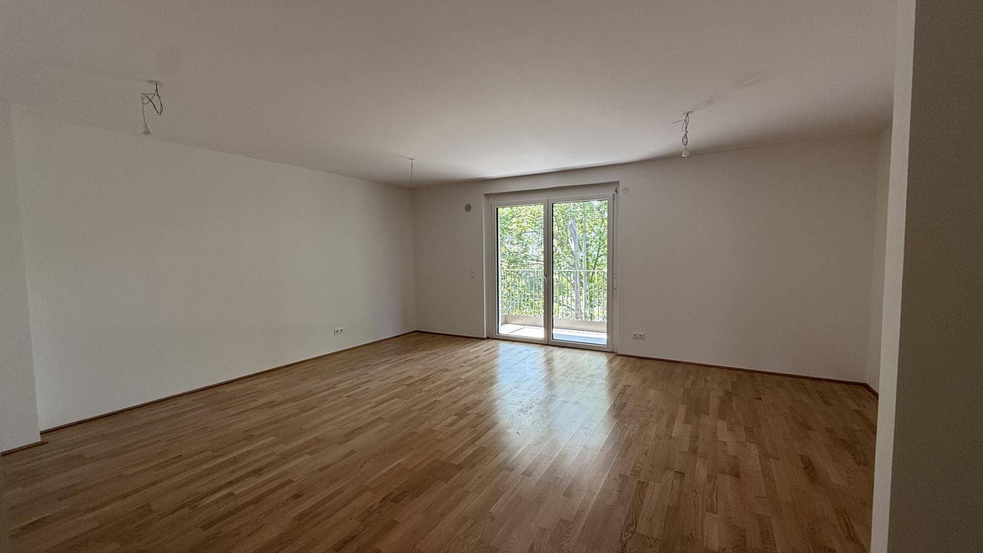 Geräumiges, helles Wohnzimmer mit Holzboden und großem Balkonzugang, bereit zur individuellen Gestaltung.