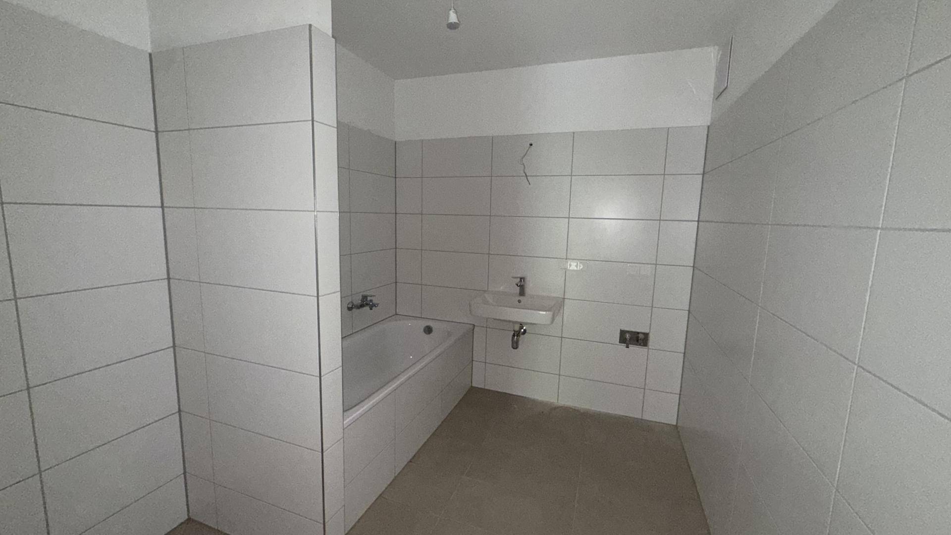 Badezimmer mit weißen Fliesen, einer Badewanne und einem Waschbecken, bereit für den letzten Ausbau.
