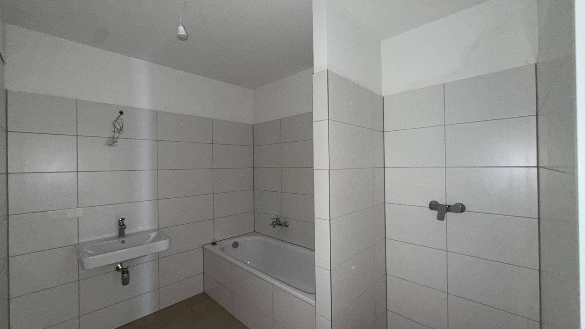 Funktionales Badezimmer mit Badewanne, Waschbecken und weißen Wandfliesen, bereit zur Einrichtung.
